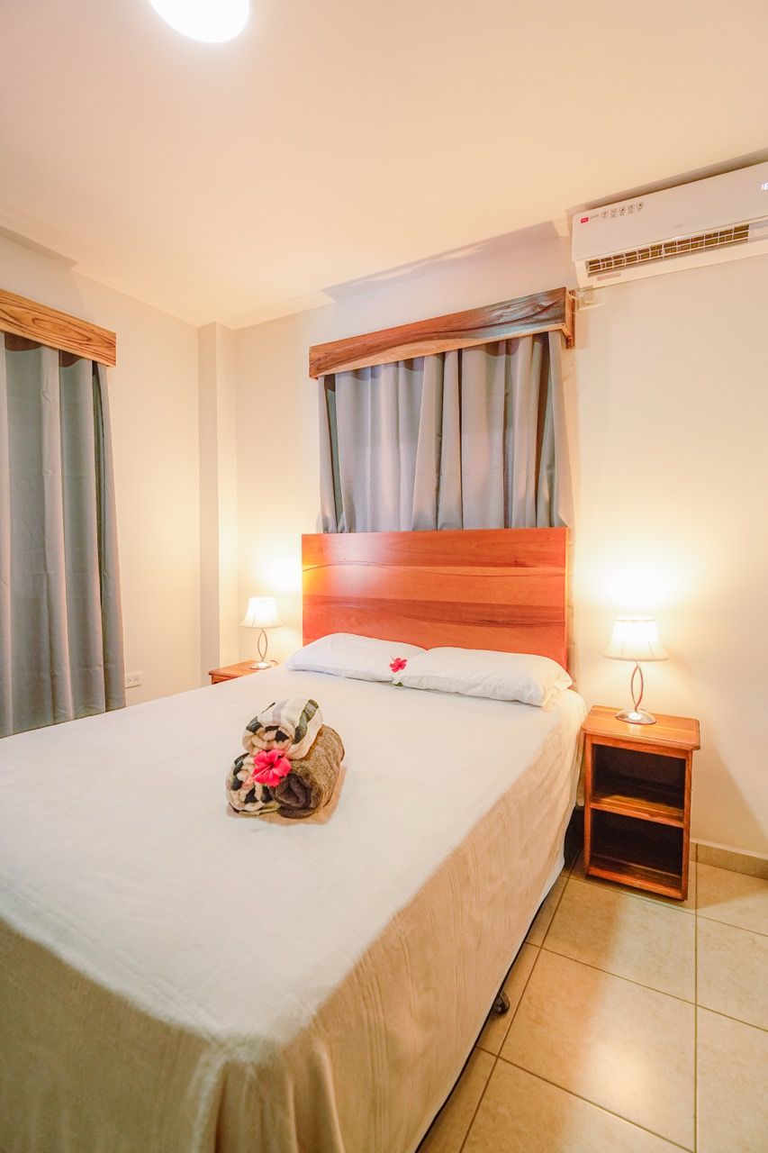Recámara con cama queen, mesitas de noche, cortinas y aire acondicionado.