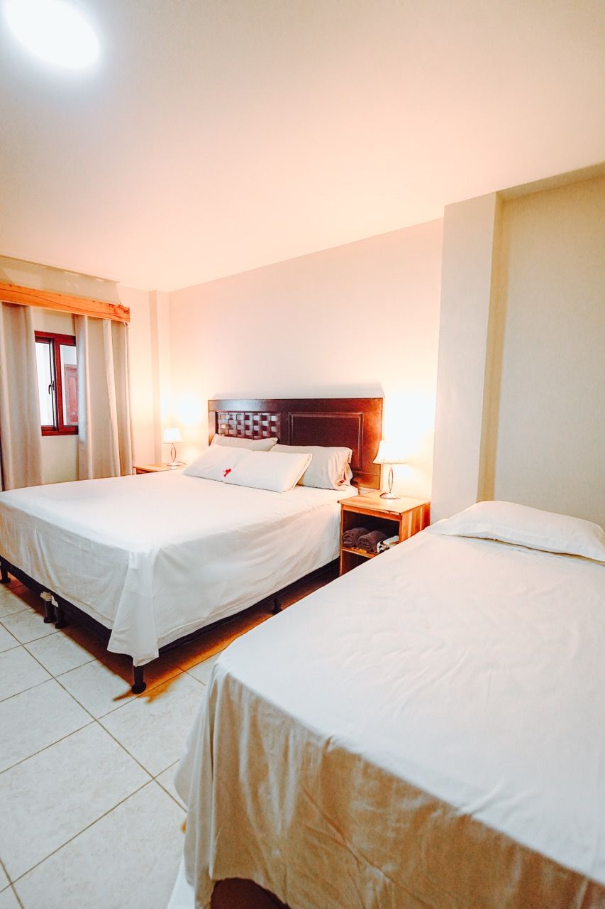 Dormitorio con una cama queen y una individual. Ambas camas tienen sábanas blancas, paredes en tonos neutros