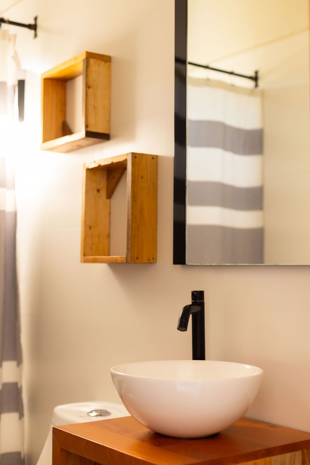 Baño con lavabo blanco, grifo negro y estantes flotantes de madera sobre una pared blanca.