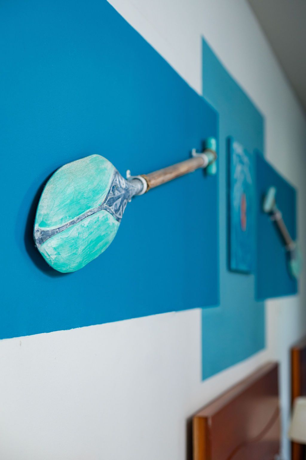 Arte de pared azul y verde azulado que presenta un remo esculpido que se extiende desde un panel azul.