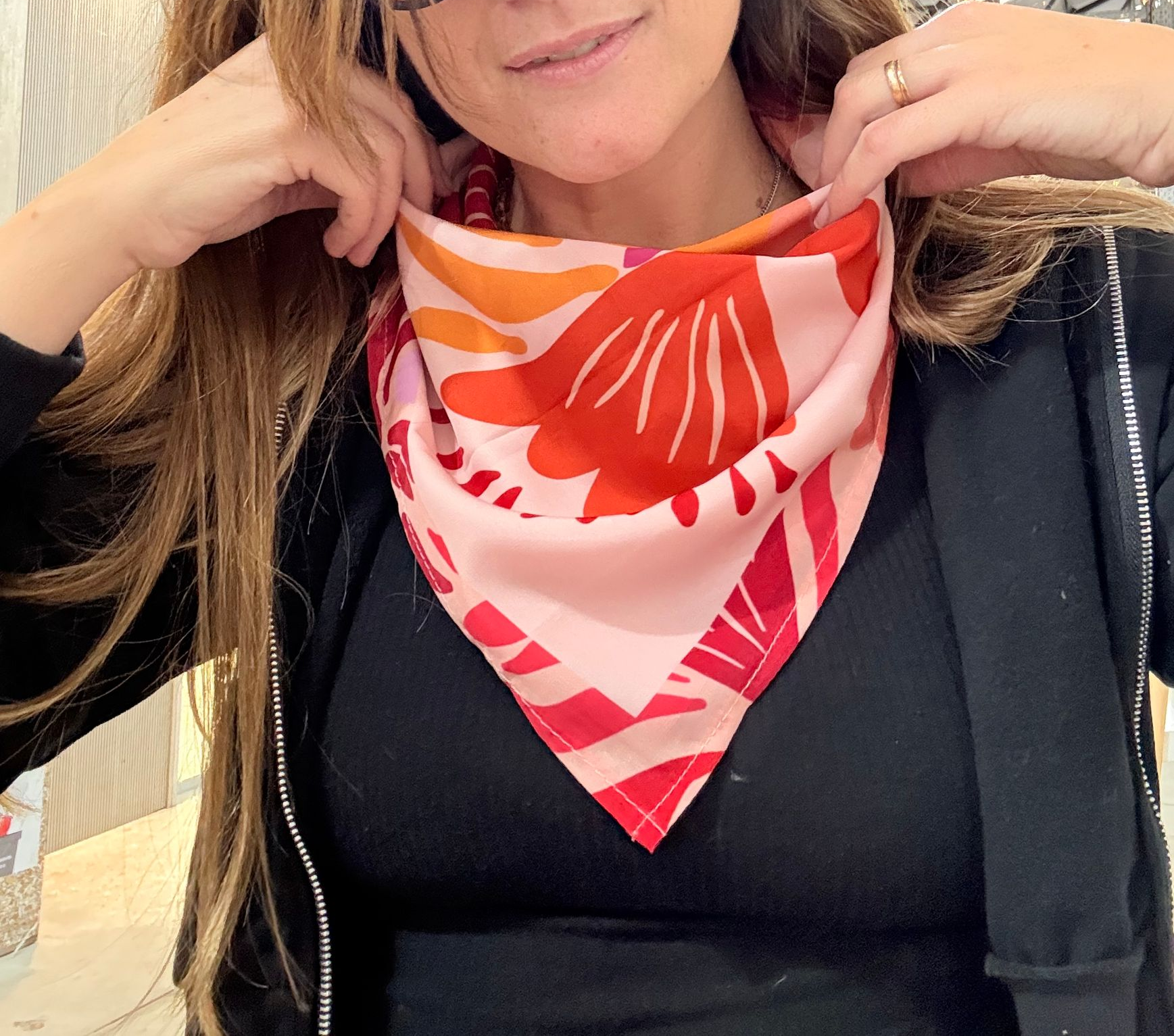 Mujer ajustándose una bufanda floral rosa alrededor del cuello, vistiendo una camisa y una chaqueta negras.