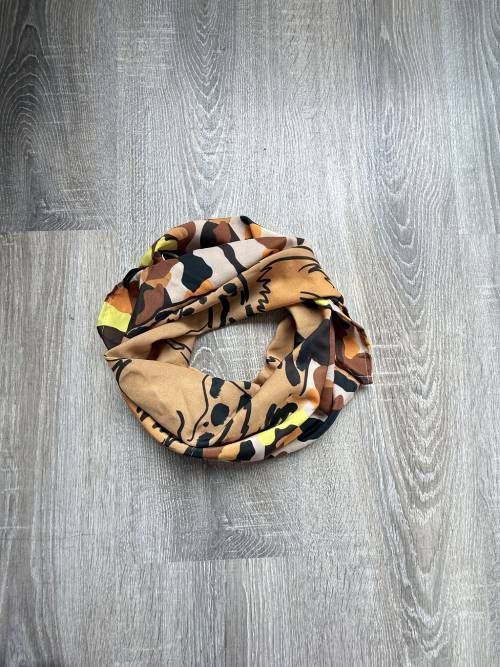 Bufanda infinita de color tostado y estampada sobre una superficie de madera gris.
