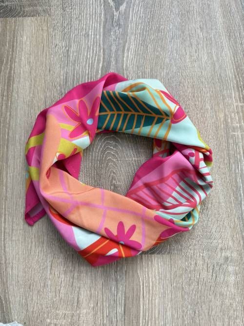 Una colorida bufanda con estampados florales se exhibe sobre una superficie de madera.