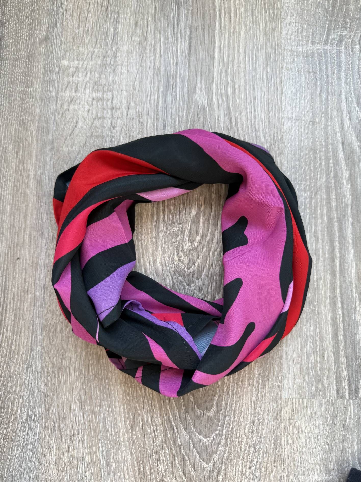 Bufanda circular con rayas de cebra negras, rojas y moradas, colocada sobre una superficie de madera.