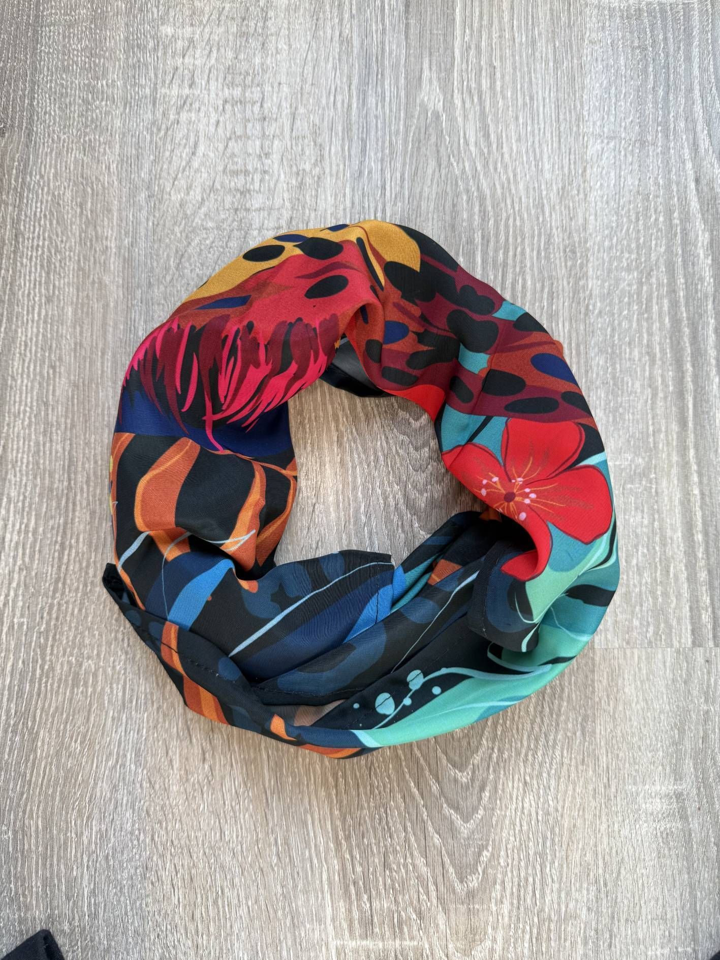 Bufanda infinita con estampado floral sobre una superficie de madera gris.