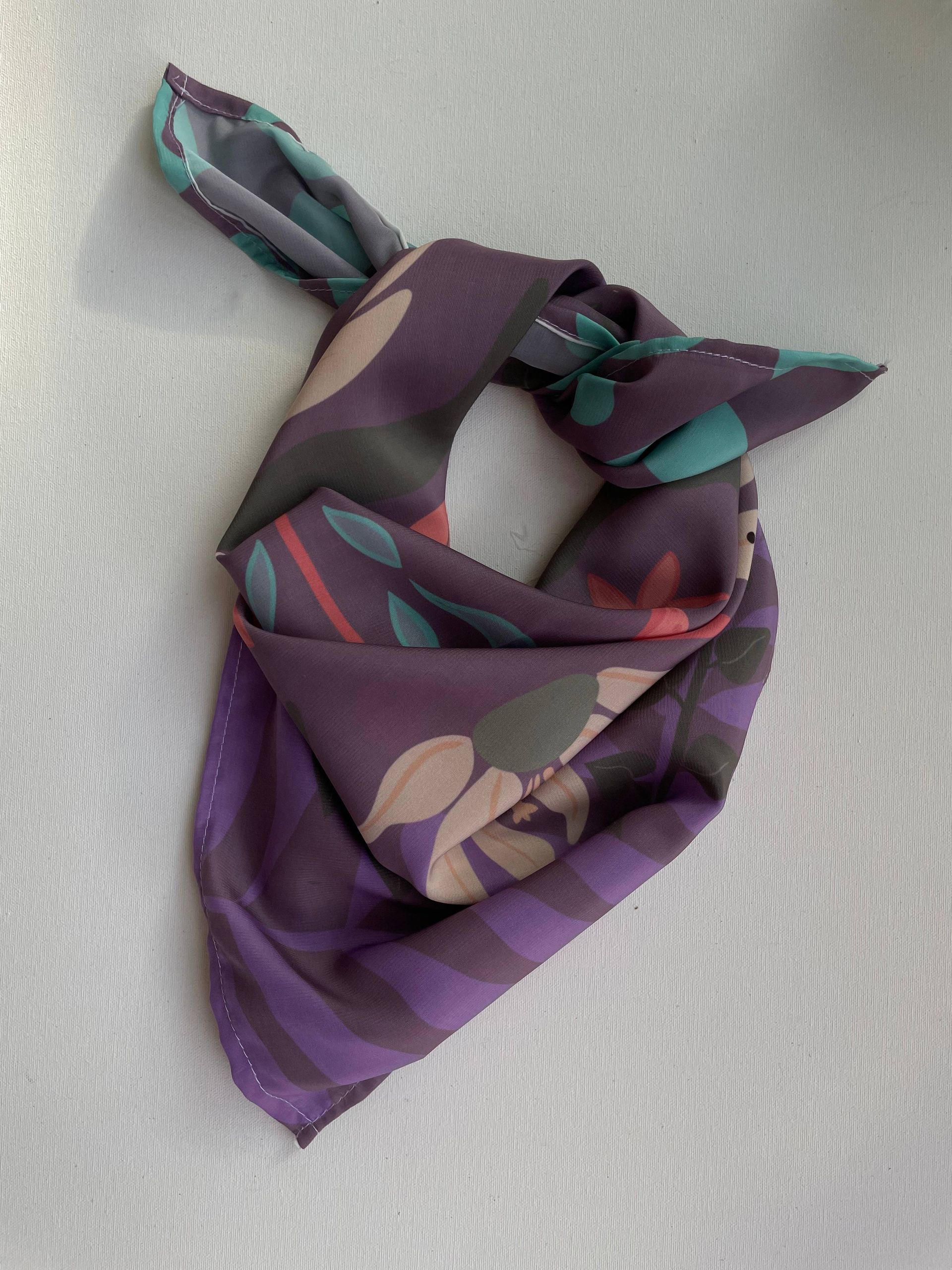 Pañuelo de seda con estampado de color morado y verde azulado atado con un nudo.