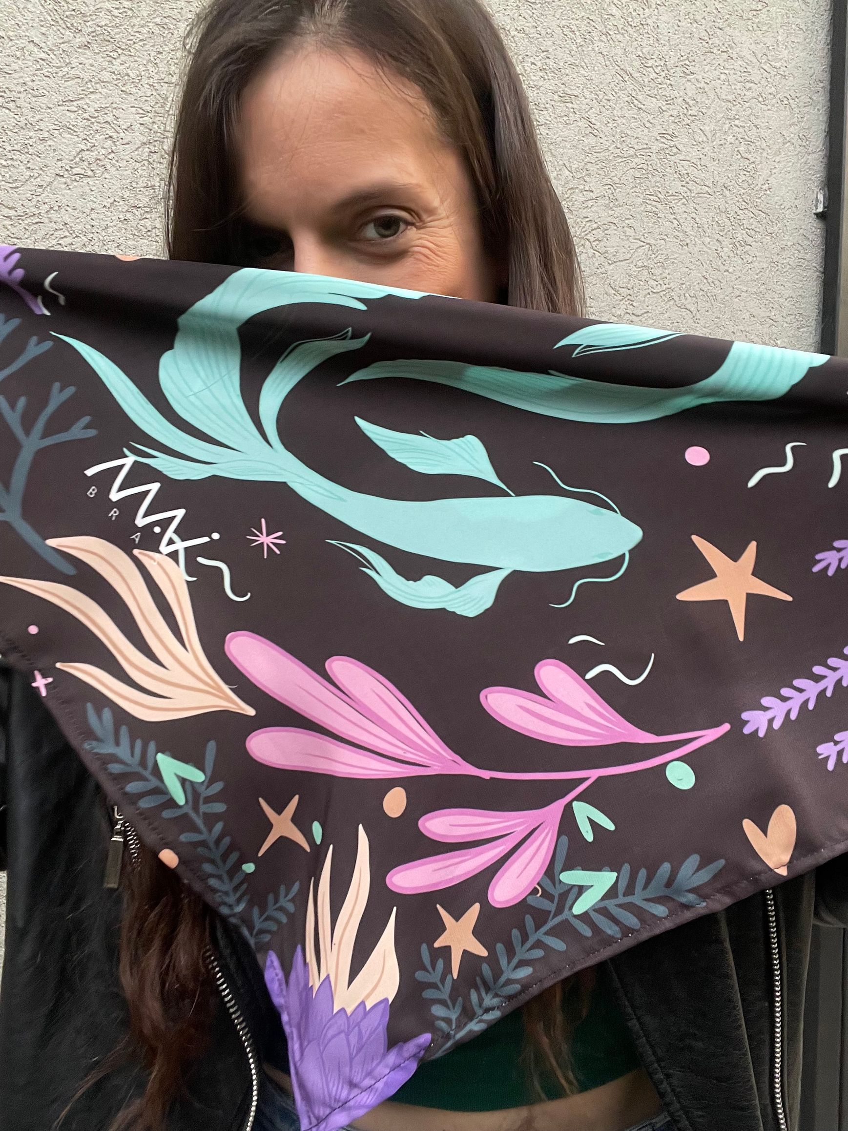 Bufanda infinita negra con estampado floral y de estrellas en verde azulado, morado y tostado sobre fondo blanco.