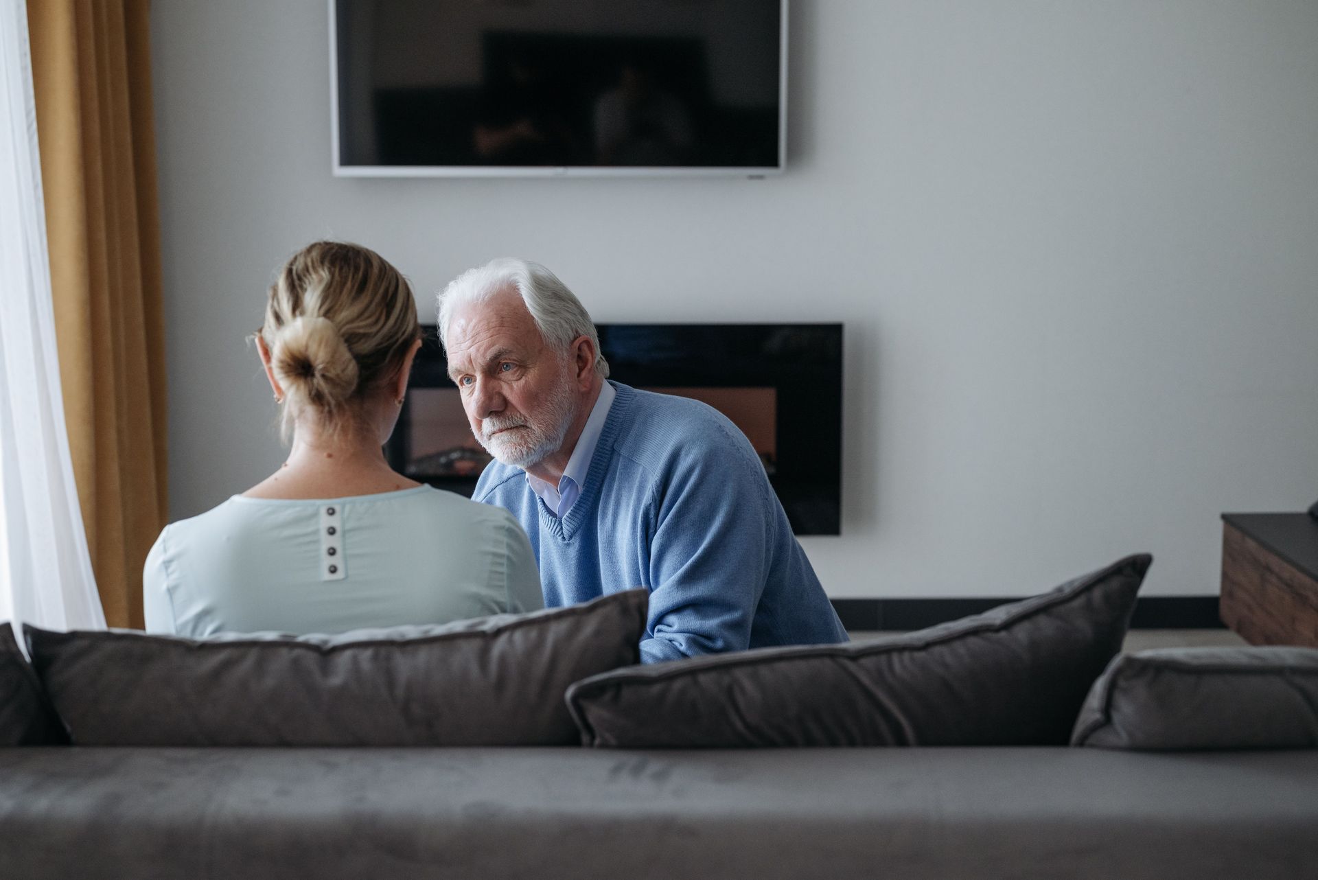 Two people seated on a couch, talking in a modern living room with a wall-mounted TV