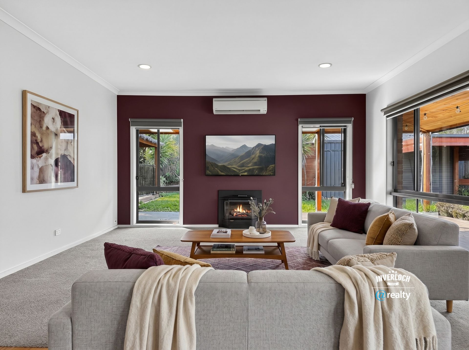 Modern living room with fireplace, wall art, large windows, gray sofa, and maroon accent wall
