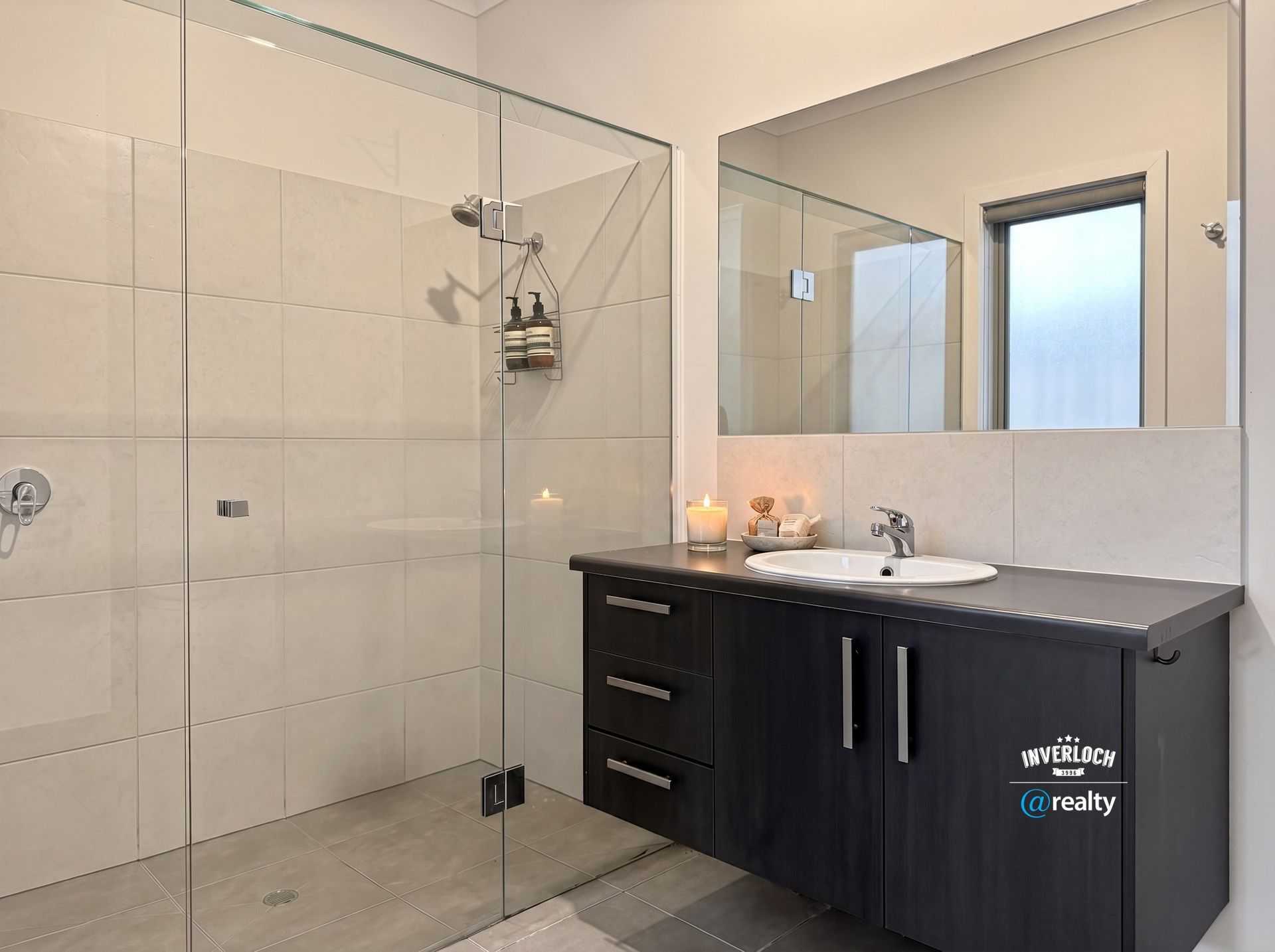 Modern bathroom with glass shower, tiled walls, and dark vanity with sink and mirror