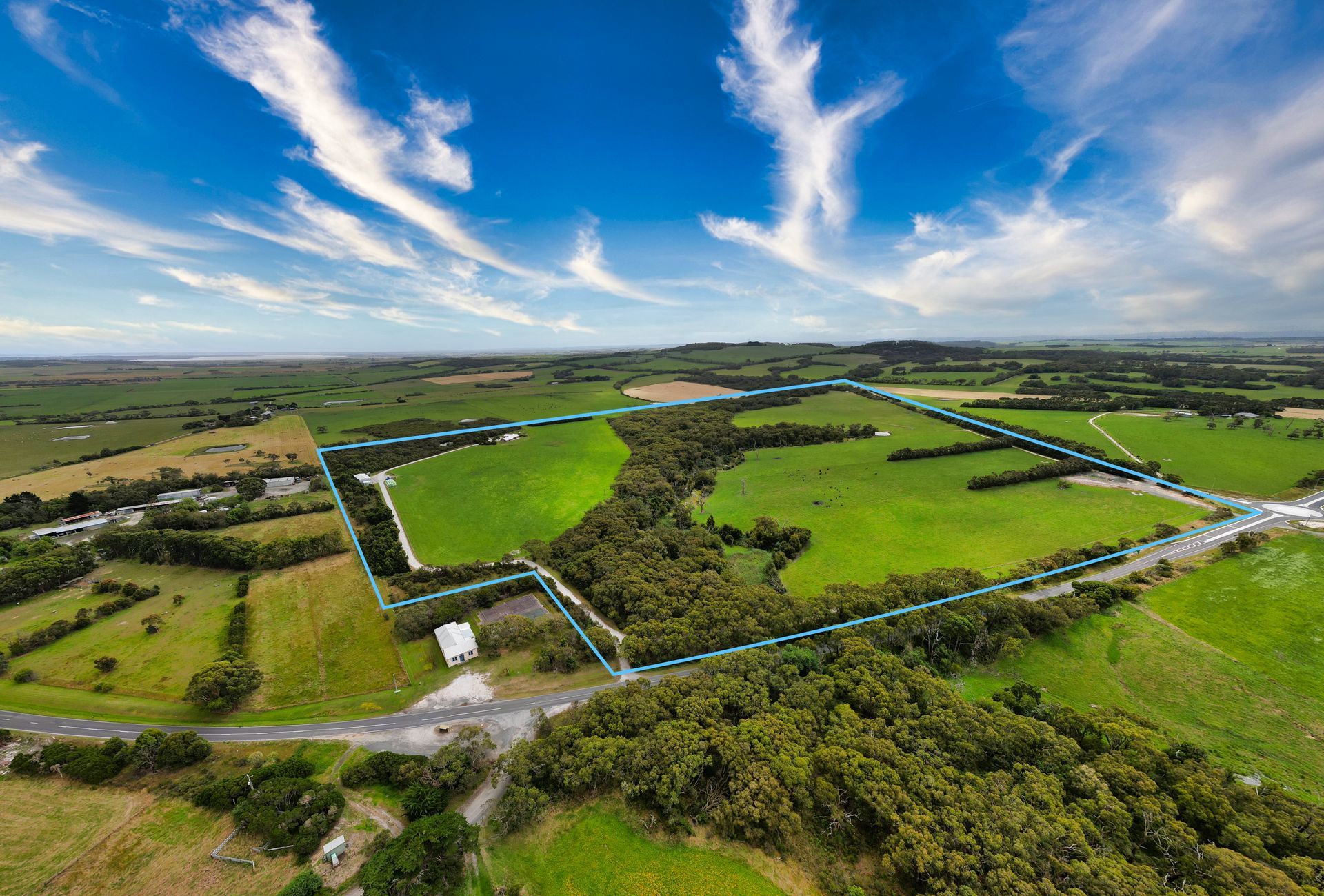 An aerial view of a large green field with trees and a road.