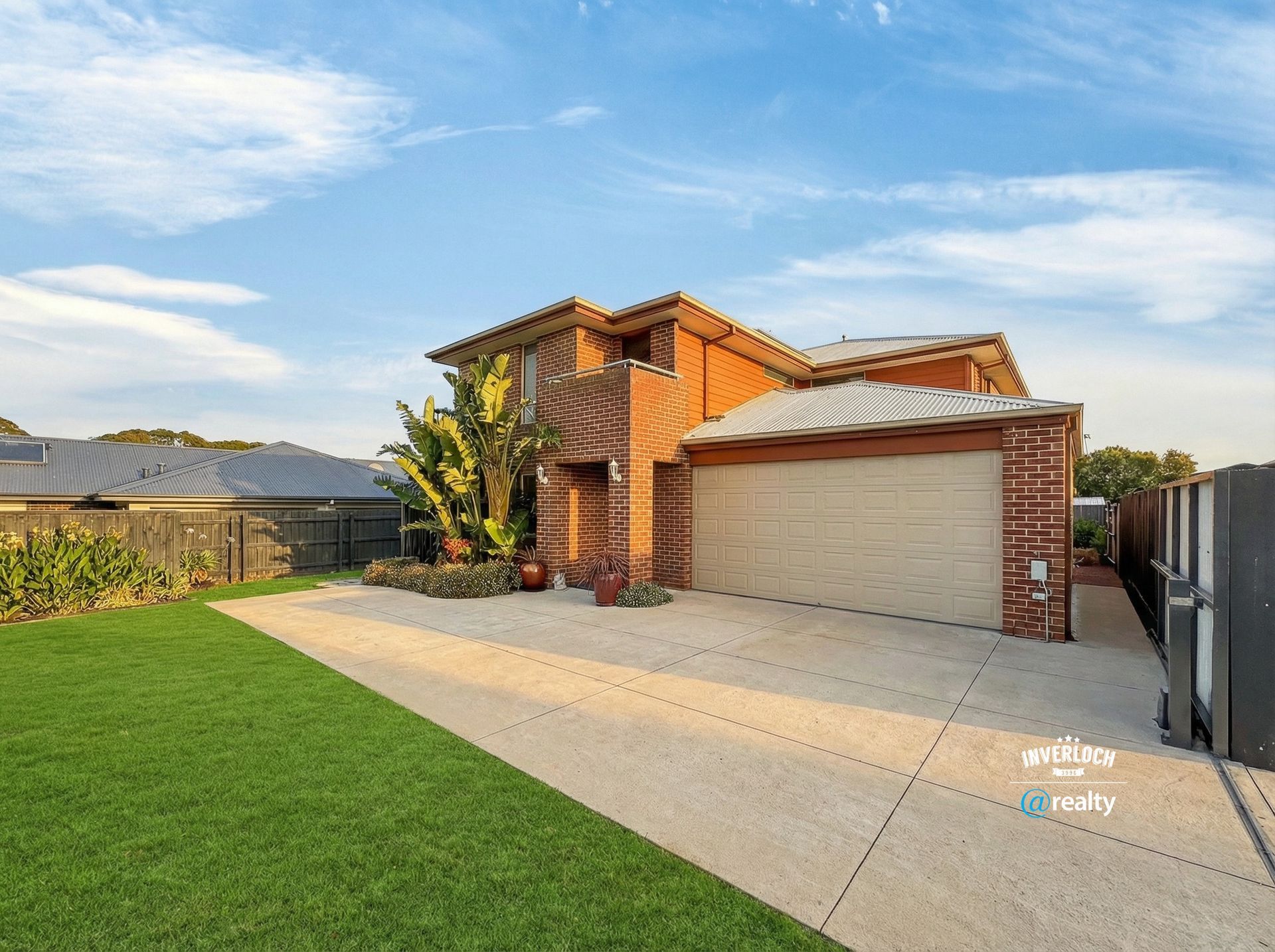 Two-story brick house with a garage and driveway on a sunny day. Green lawn and blue sky.