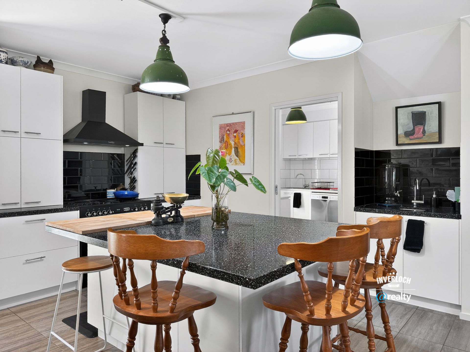 Kitchen with white cabinets, black countertops, wooden stools, and green pendant lights.