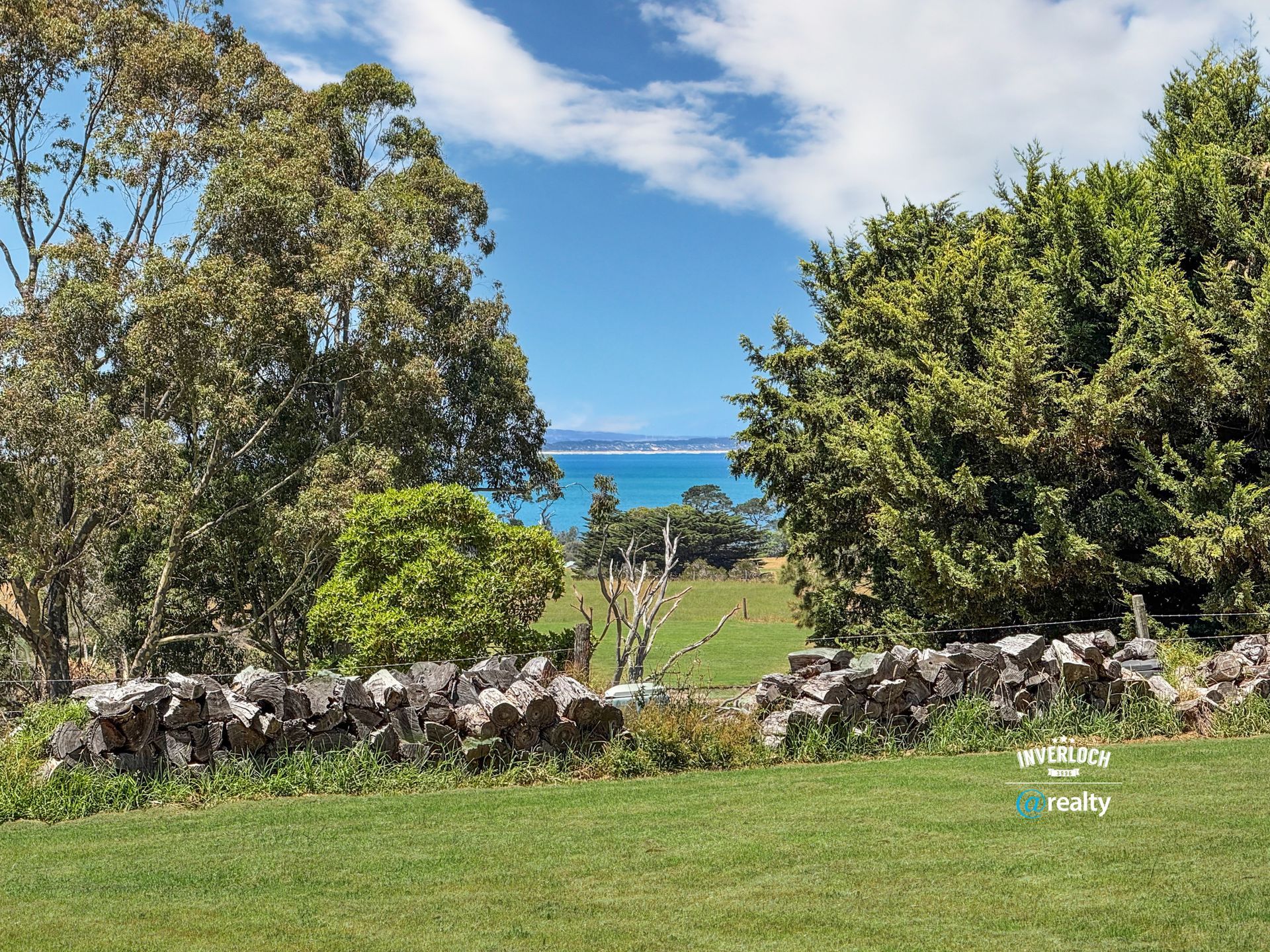 A stone wall surrounds a grassy field with trees and a view of the ocean.