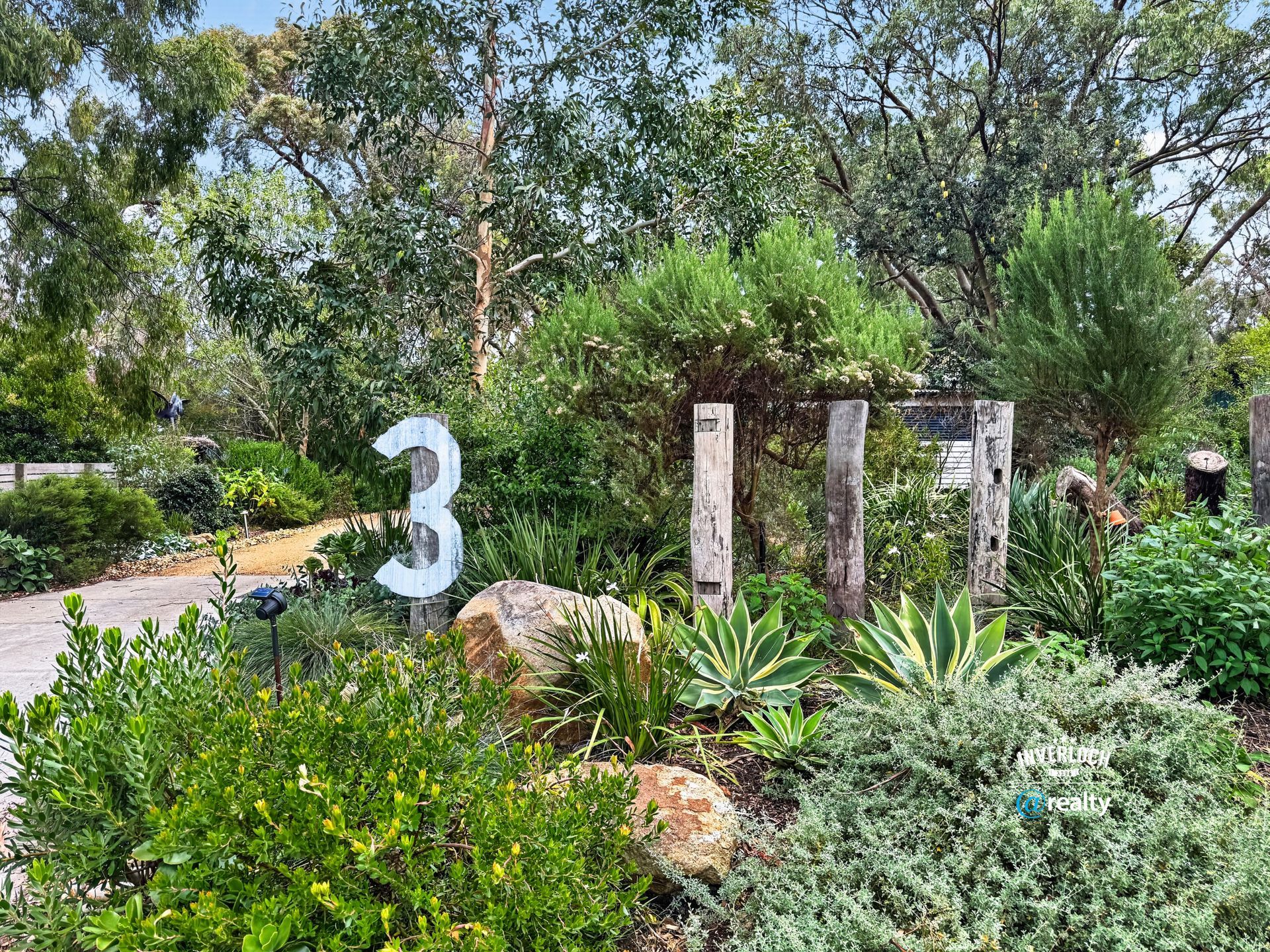 Large white “3” beside stone pillars and lush green landscaping in a garden path area