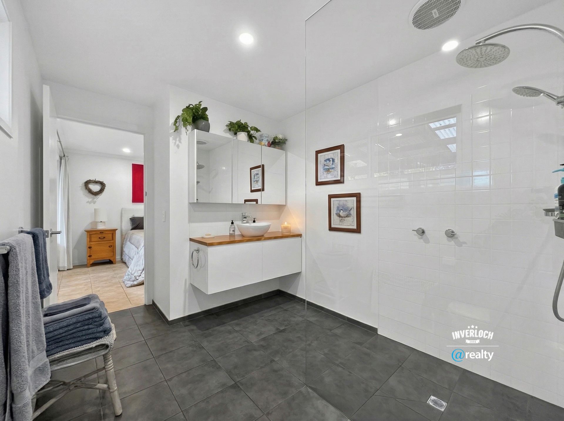 Bright modern bathroom with white tile, walk-in shower, floating vanity, dark floor, and plants.