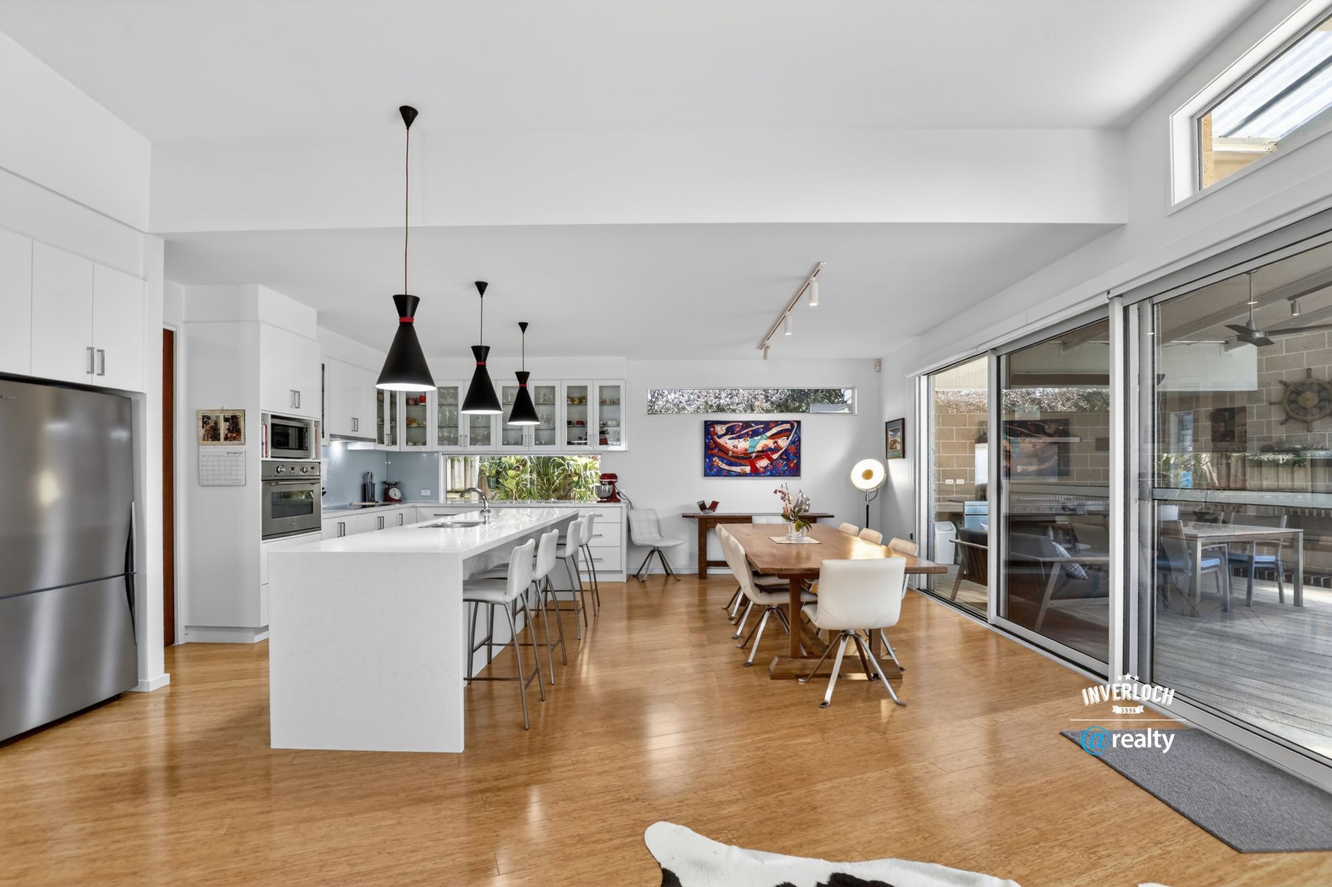 Modern open-plan kitchen and dining area with white cabinets, island, and dining table, with large sliding glass doors.