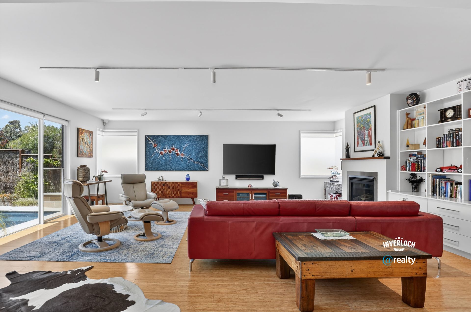 Spacious living room with red sofa, wood floor, blue rug, and modern decor near a pool.