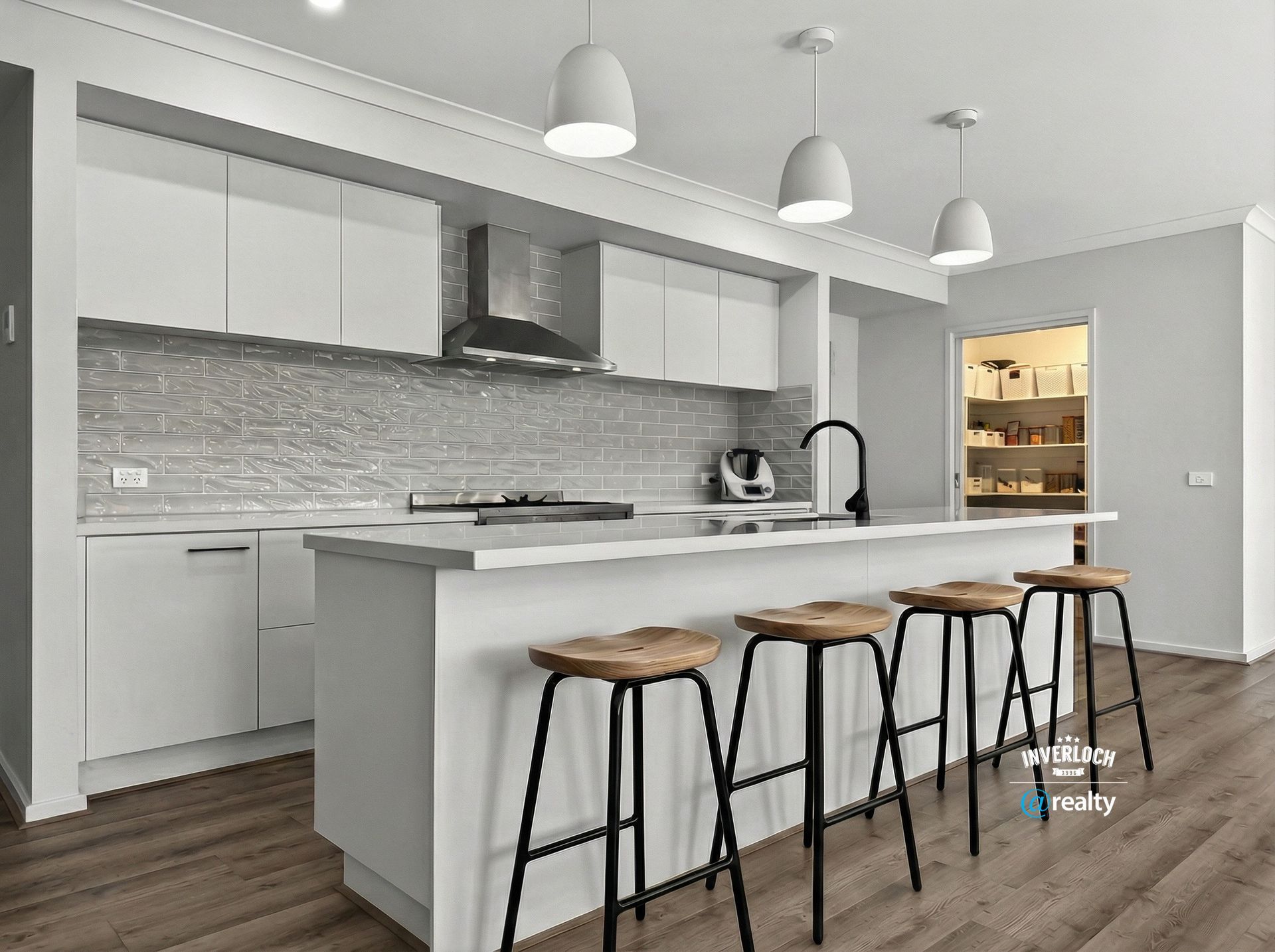 Modern white kitchen with island, stools, pendant lights, and stainless steel appliances.