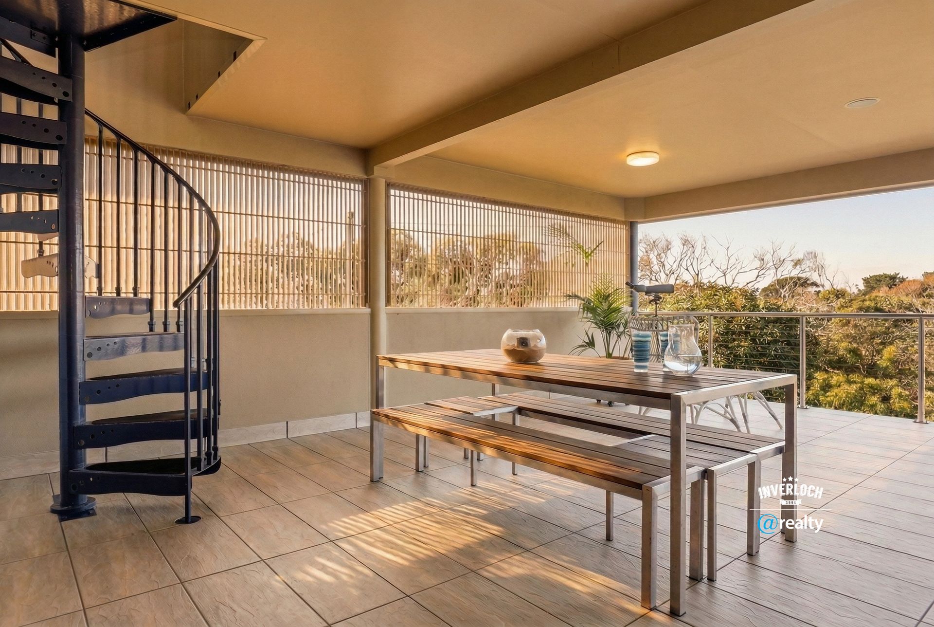 Covered patio with spiral staircase, long wooden table, and sunset view through open railings.
