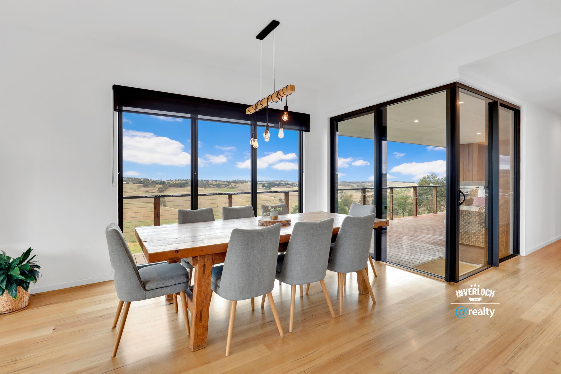 Dining room with a wooden table, eight grey chairs, and a view of a landscape.