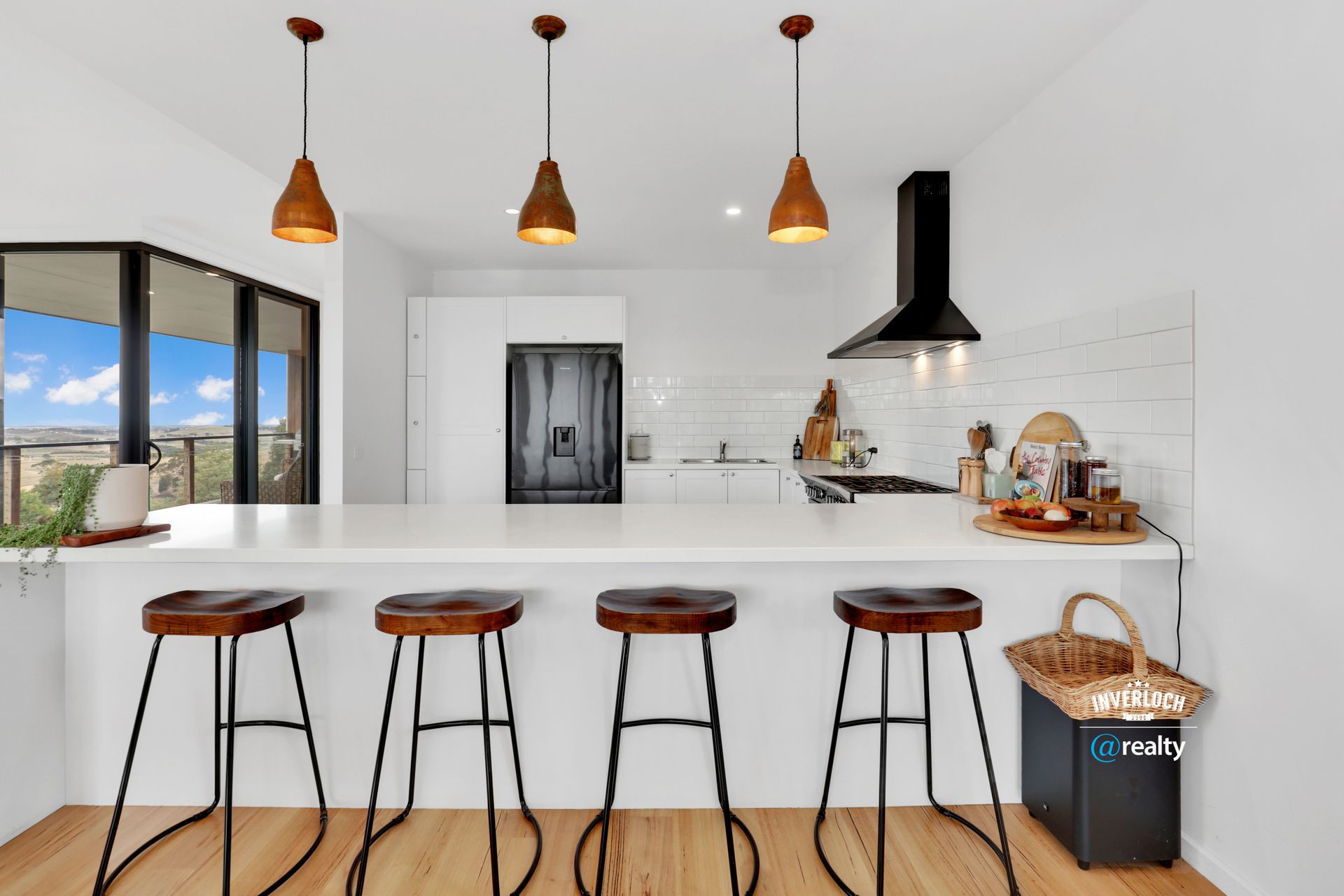 Kitchen with white counters, wooden stools, and three pendant lights above a breakfast bar.