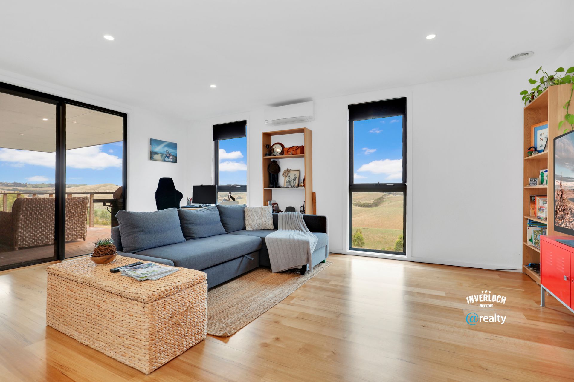 Living room with blue sectional, woven ottoman, windows overlooking a rural landscape.