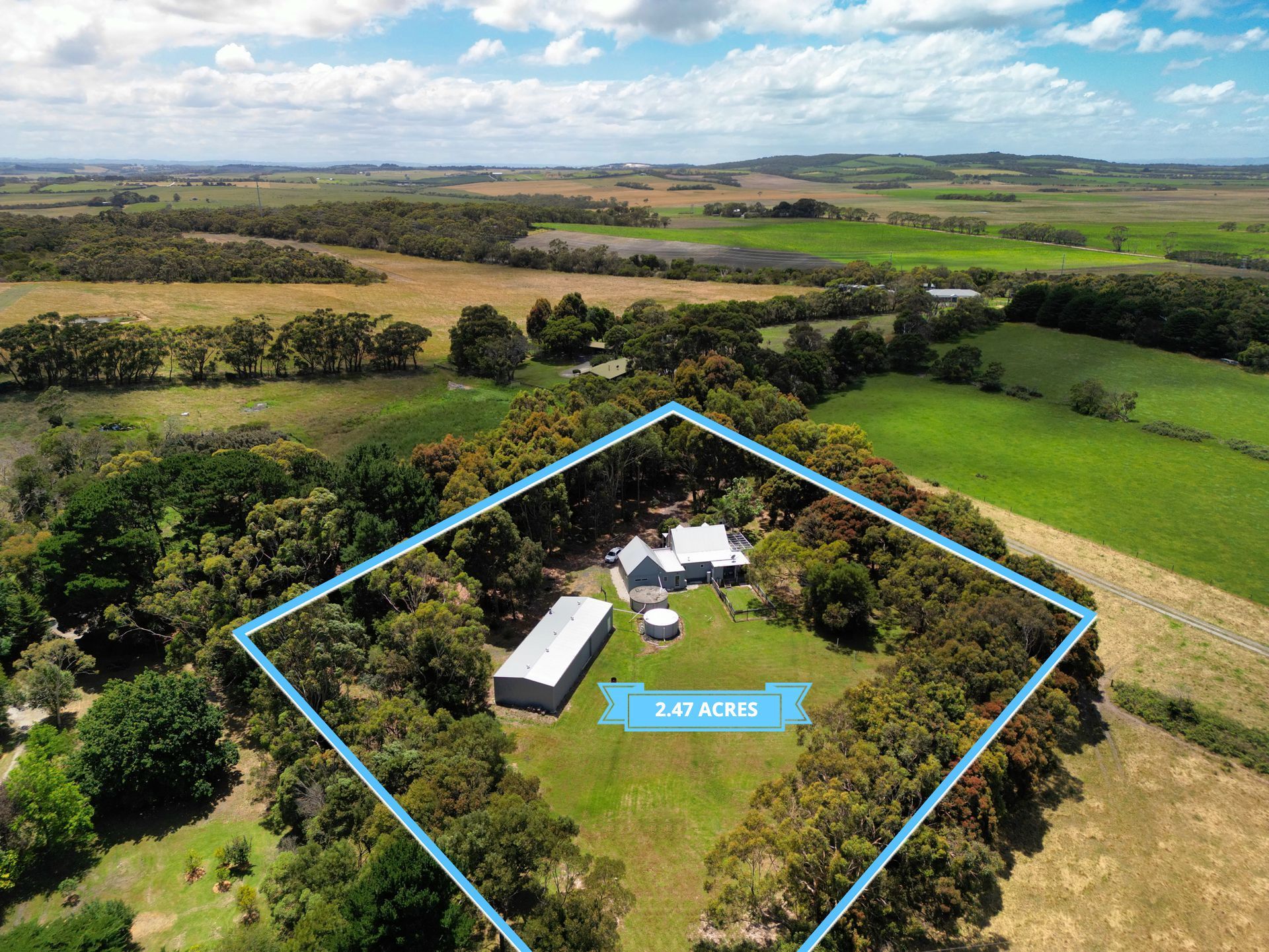 An aerial view of a house in the middle of a field surrounded by trees.