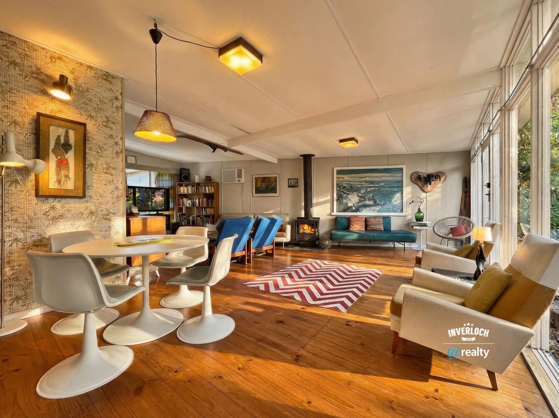 Bright, airy living room with a dining area, fireplace, and large windows. Sunlight streams in, illuminating furniture and art.