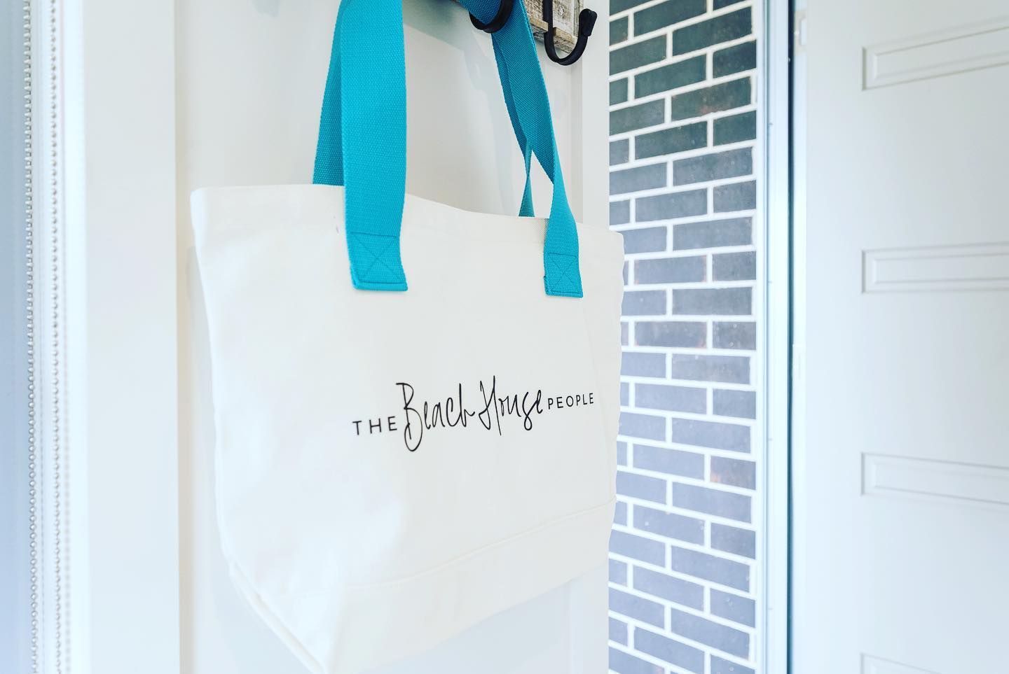 A white tote bag with blue handles is hanging on a door.