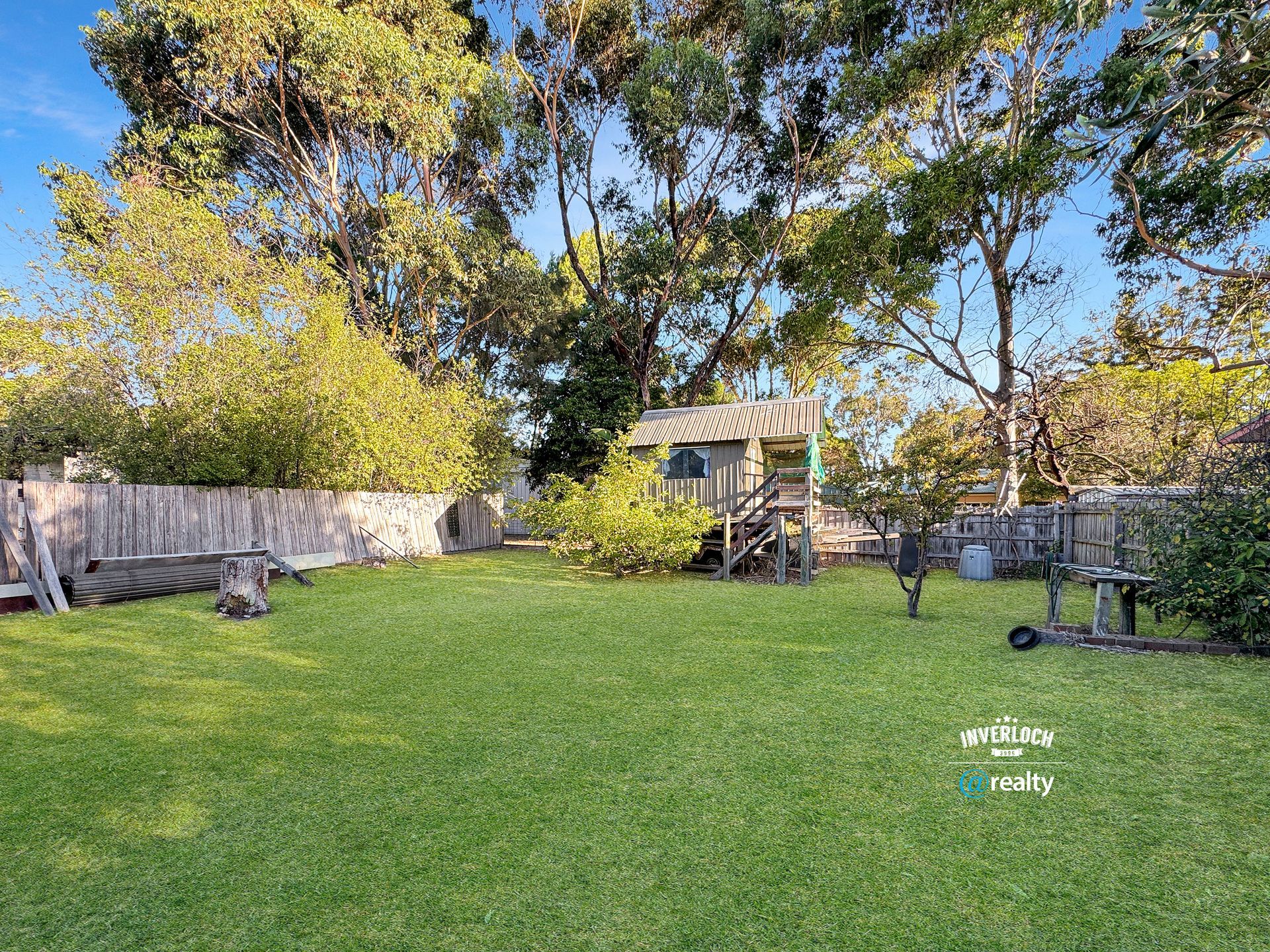A backyard with a fence , trees and a playhouse.