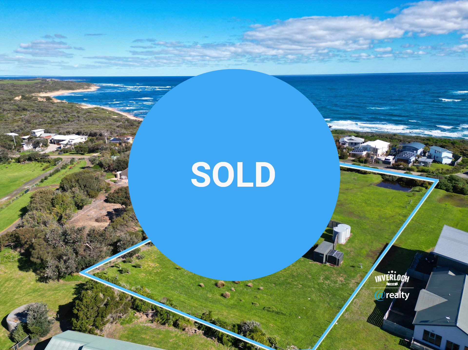 Aerial view of a house on a large grassy lot near the ocean. Blue outlined property with solar panels.