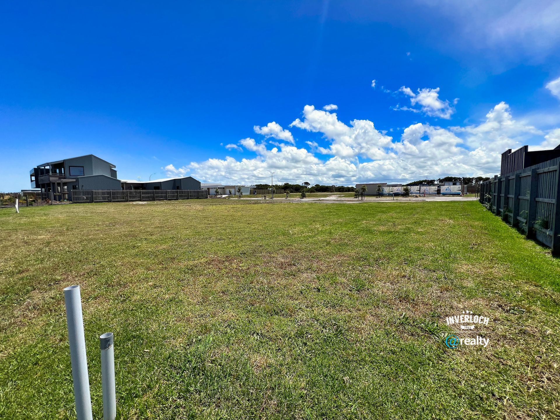 A large grassy field with a fence and a house in the background.