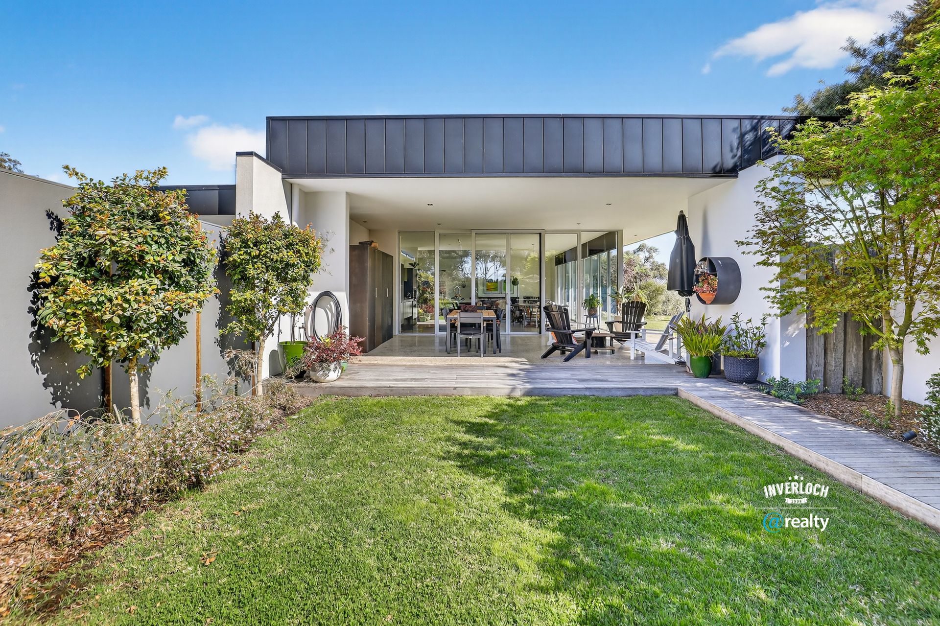 Exterior of a modern home with a covered patio, featuring green lawn, white walls, and glass doors.