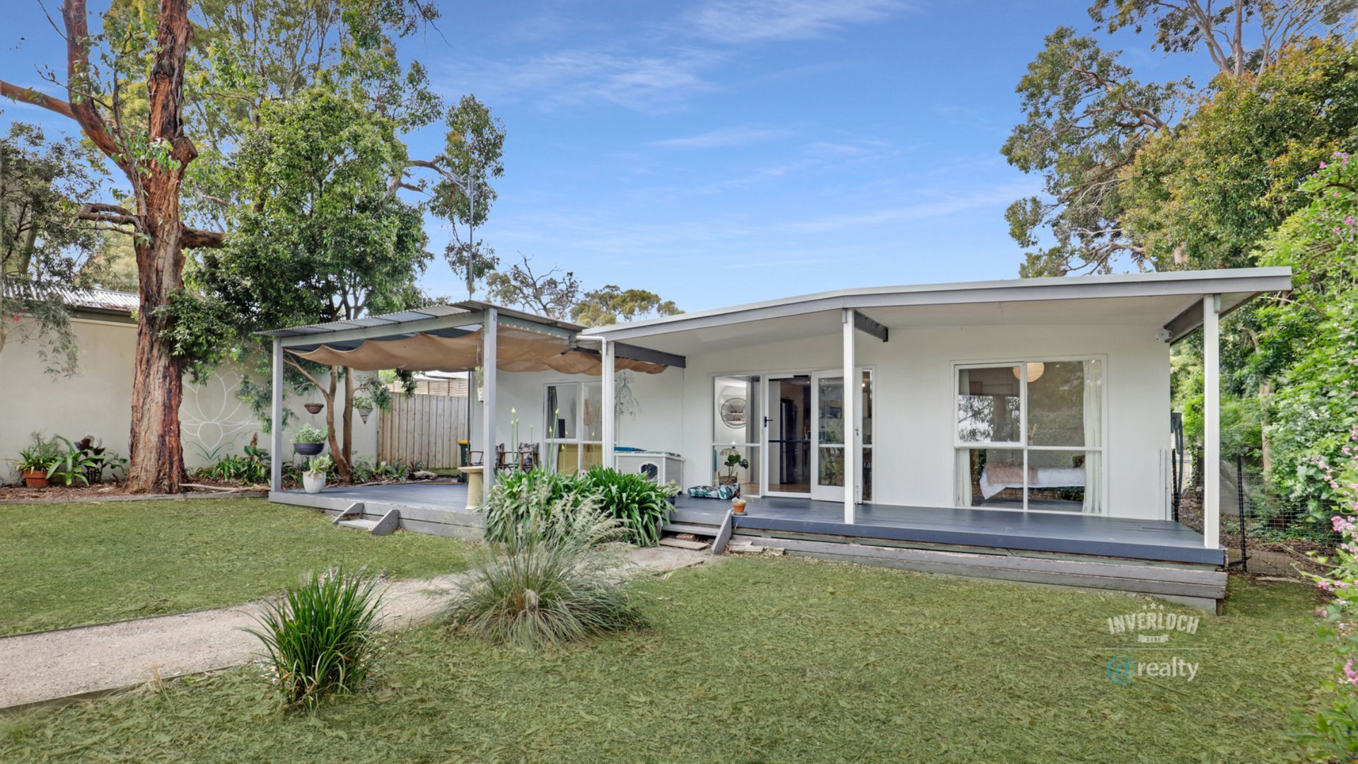 Modern white house with a covered patio, glass doors, and a green backyard lawn under blue sky