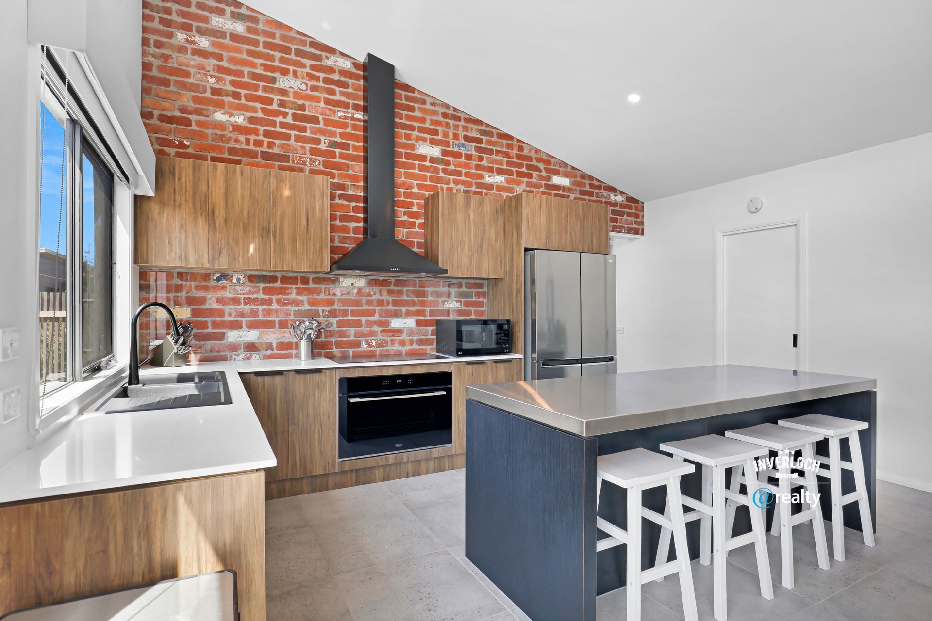 A kitchen with a large island and stools and a brick wall.