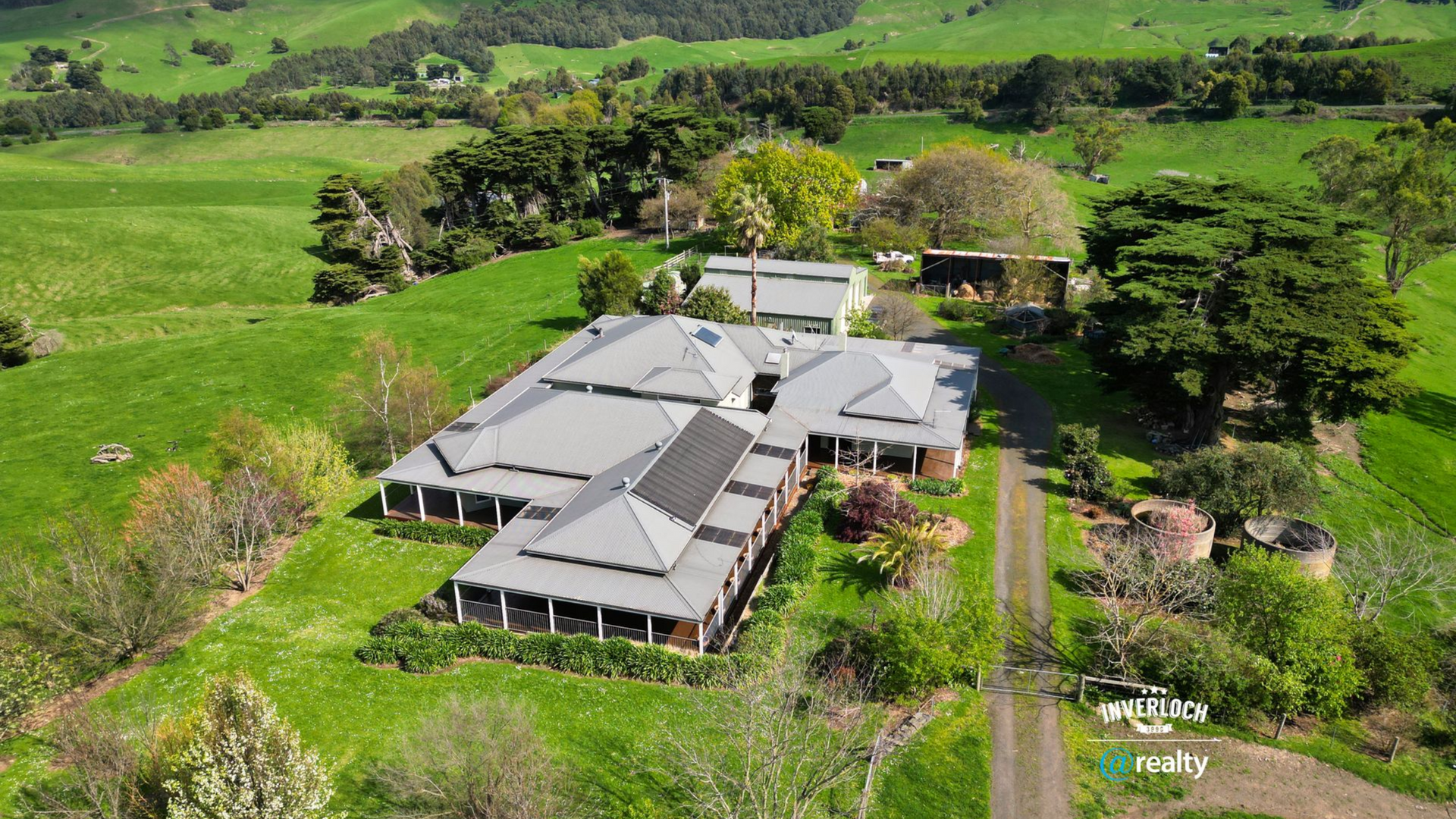 Aerial view of a rural lodge with gray roofs amid lush green fields and trees.