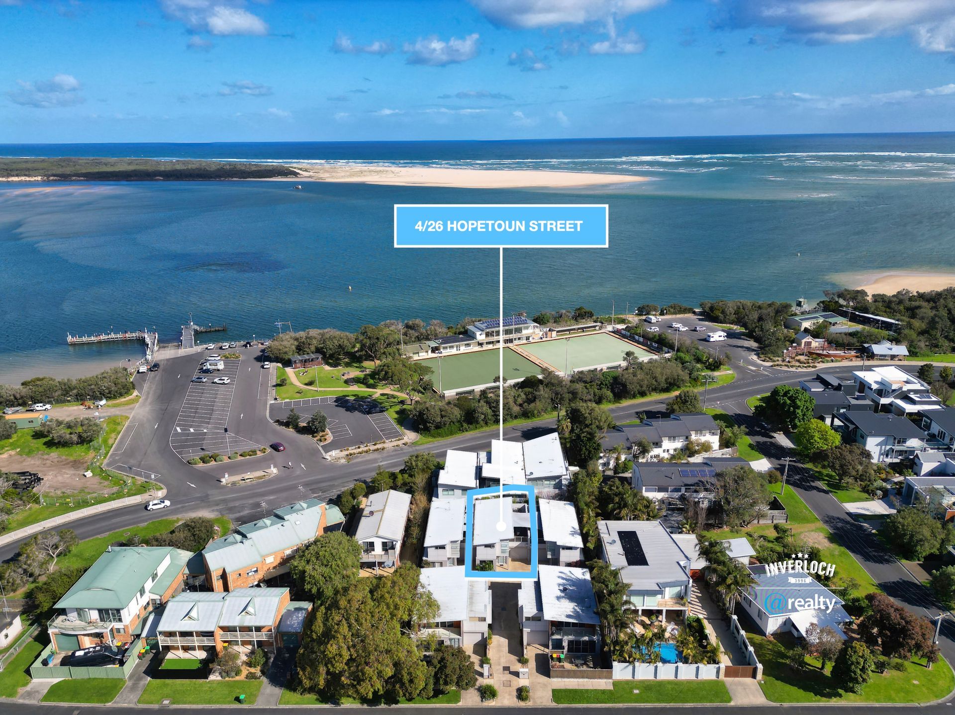 Aerial view of coastal homes beside a road and blue ocean under a partly cloudy sky