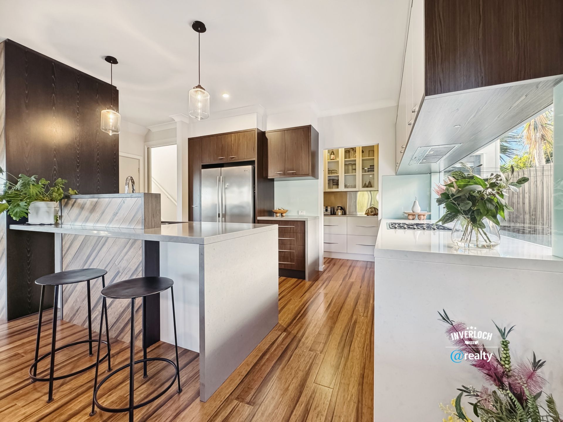 A kitchen with wooden floors , stools , a refrigerator and a sink.