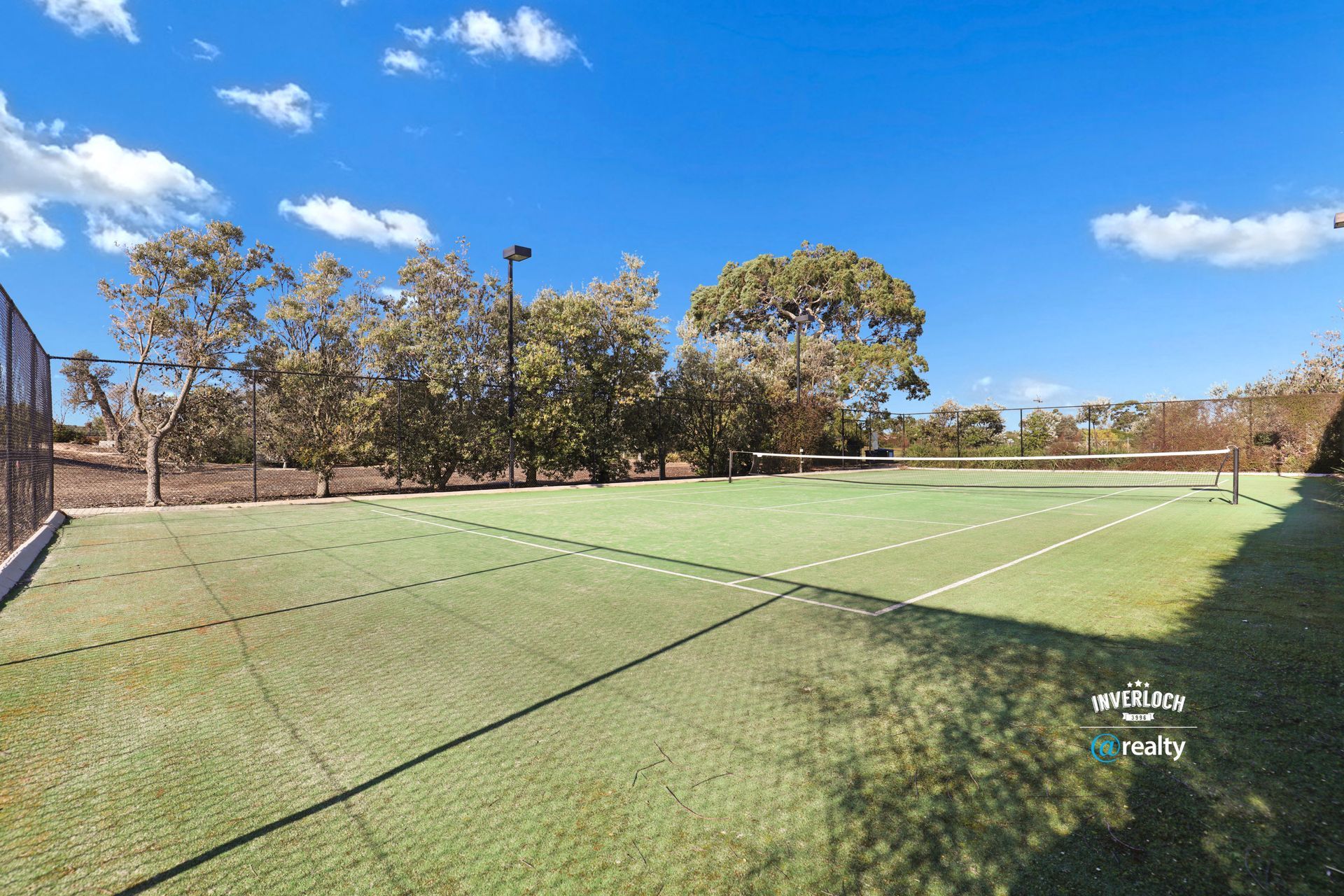 A tennis court with a fence and trees in the background on a sunny day.