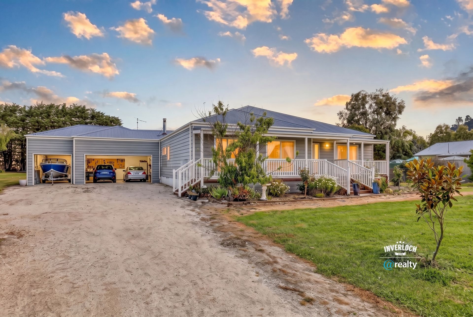 Single-story home with lit garage, front porch, gravel drive, and sunset sky