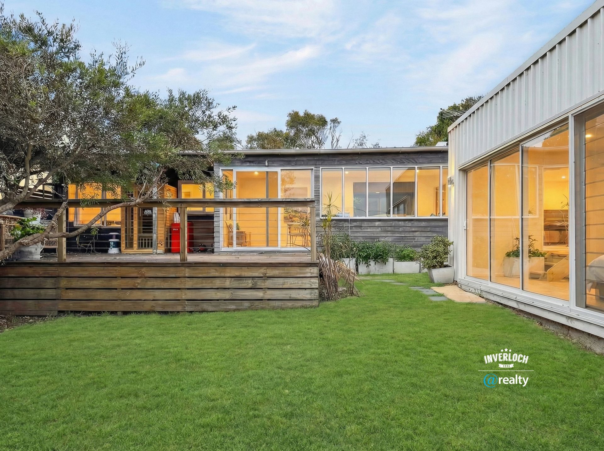 A backyard features a wooden deck and a lush lawn, bordered by a modern home with large glass sliding doors.