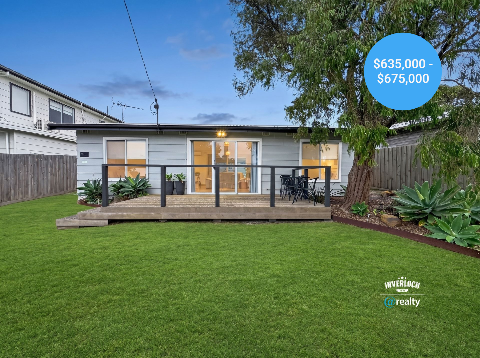Modern single-story house with sliding doors, wooden deck, and a large green lawn at dusk