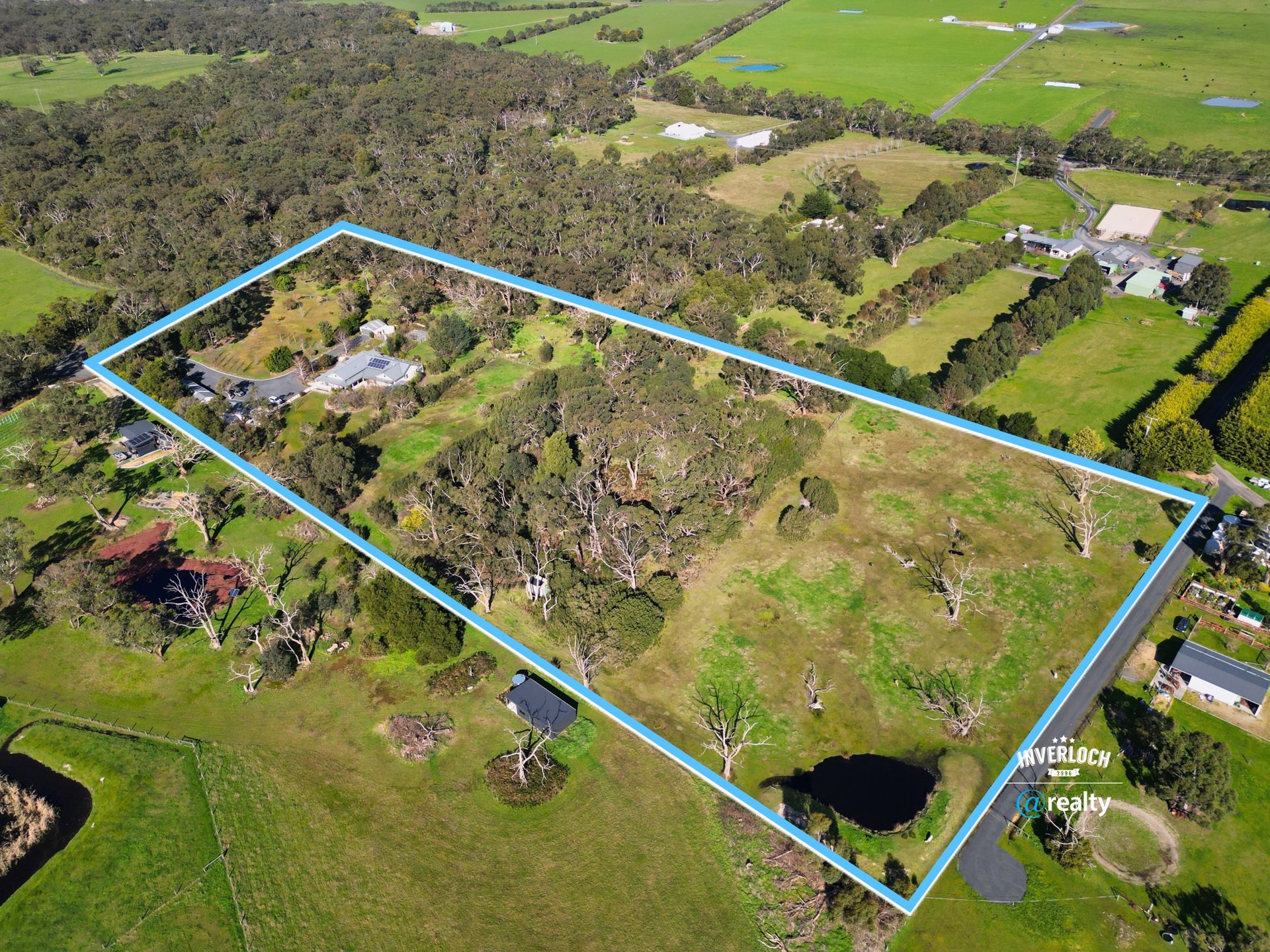 Aerial view of a fenced rural property with a house, trees, lawns, and surrounding farmland