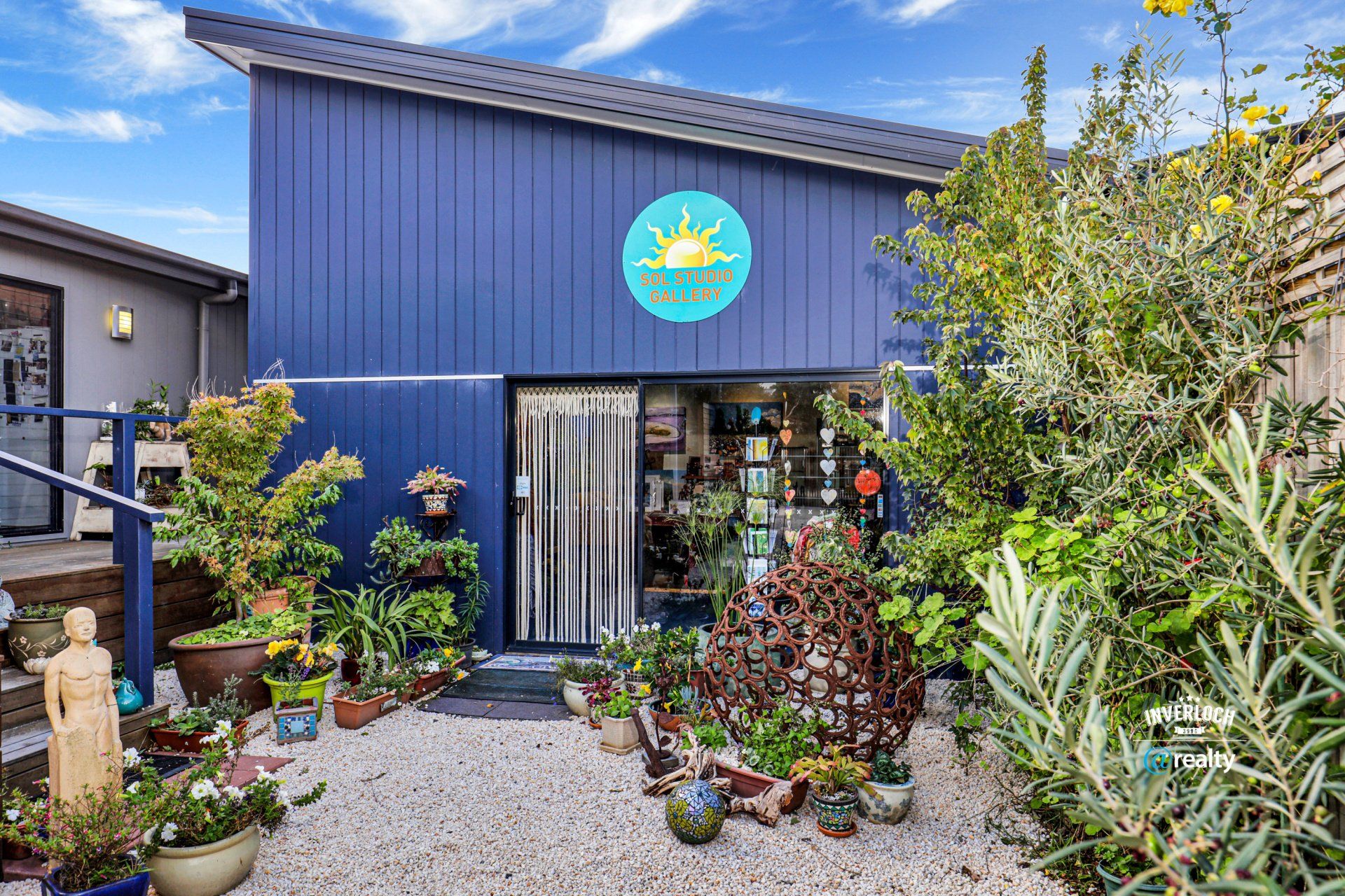 A blue building with a sun on it is surrounded by potted plants.