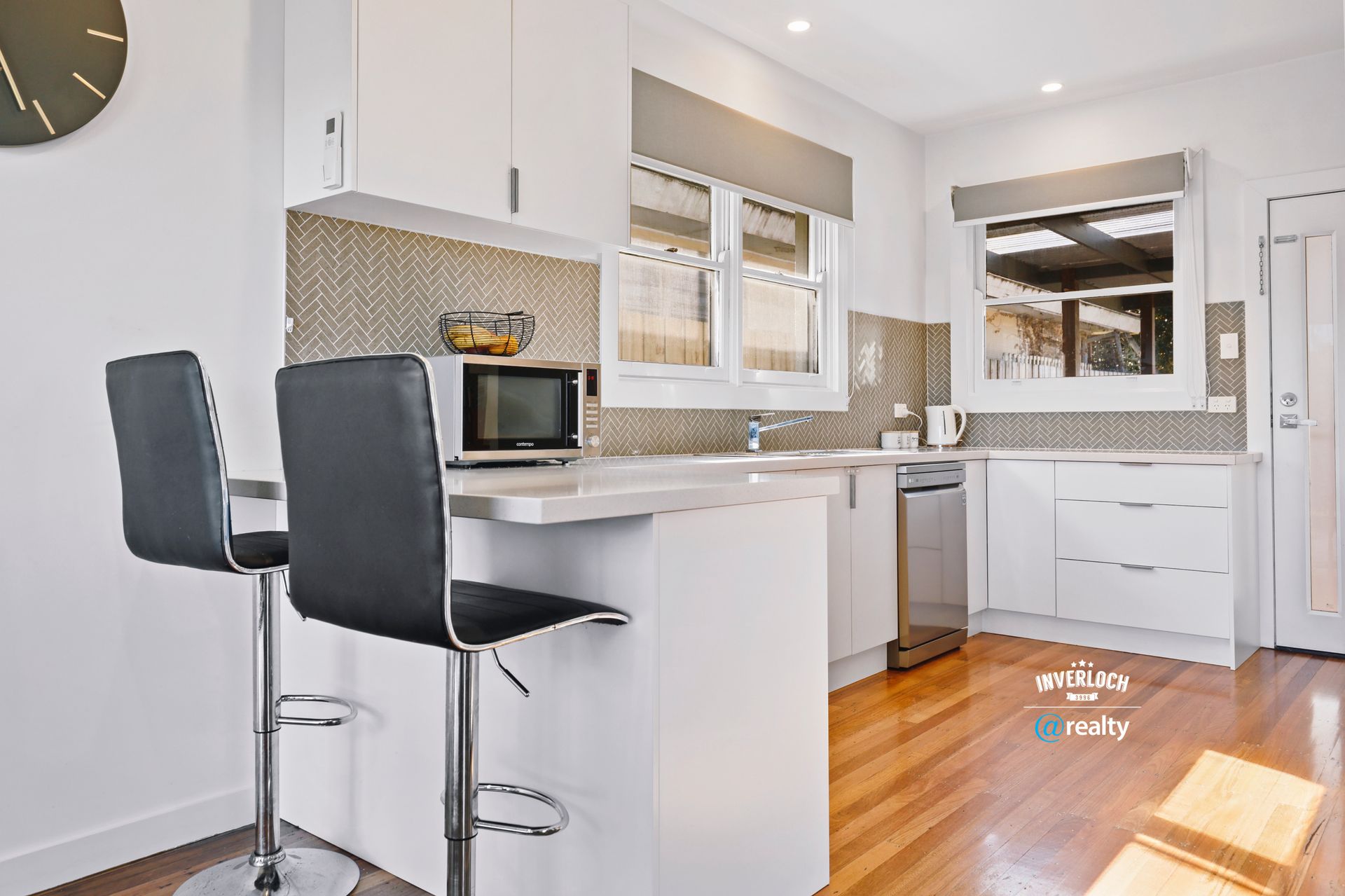 A kitchen with two bar stools and a clock on the wall.
