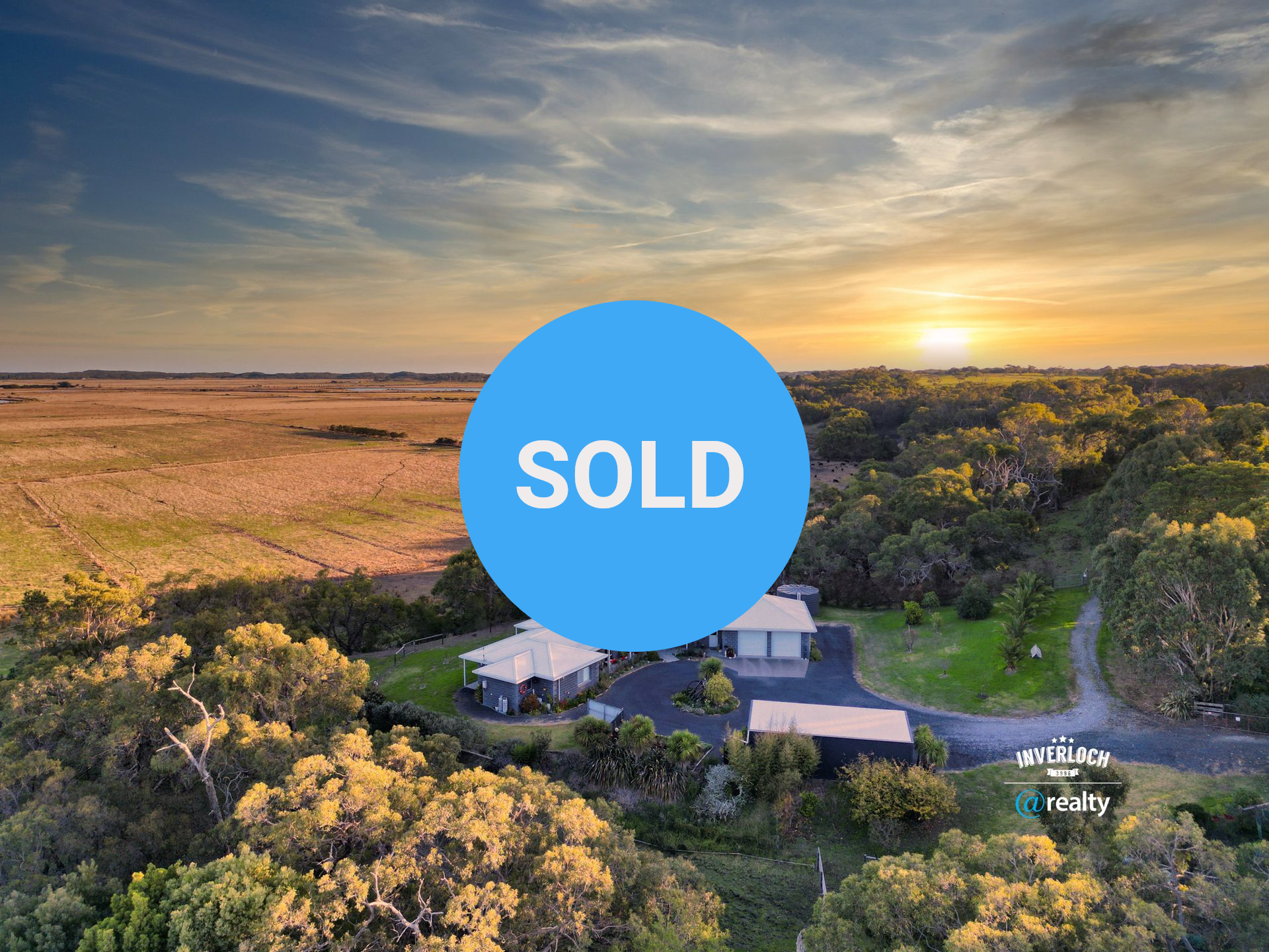 An aerial view of a house in the middle of a field at sunset.