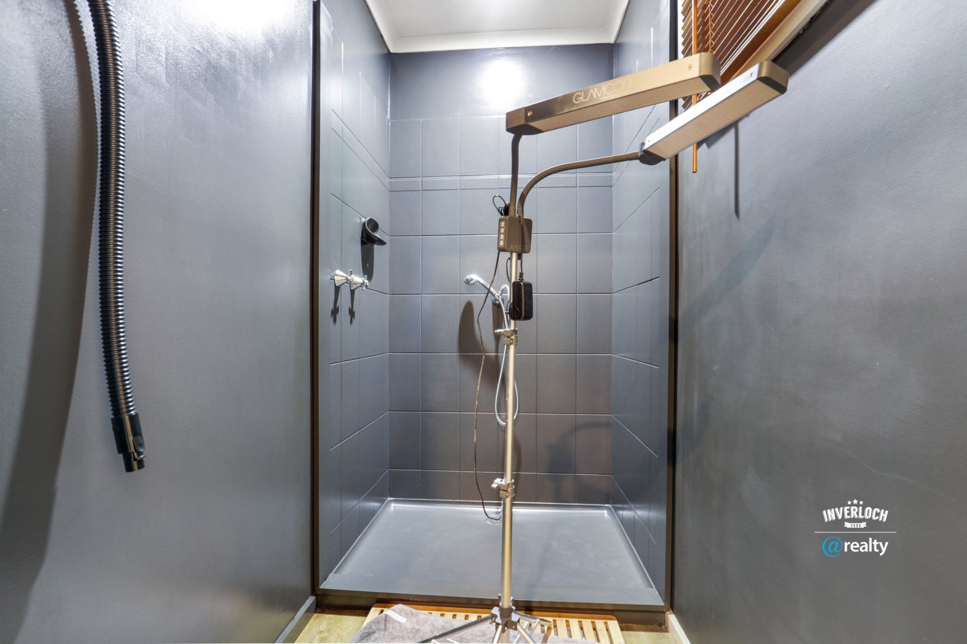 A bathroom with a walk in shower and a hose hanging from the ceiling.
