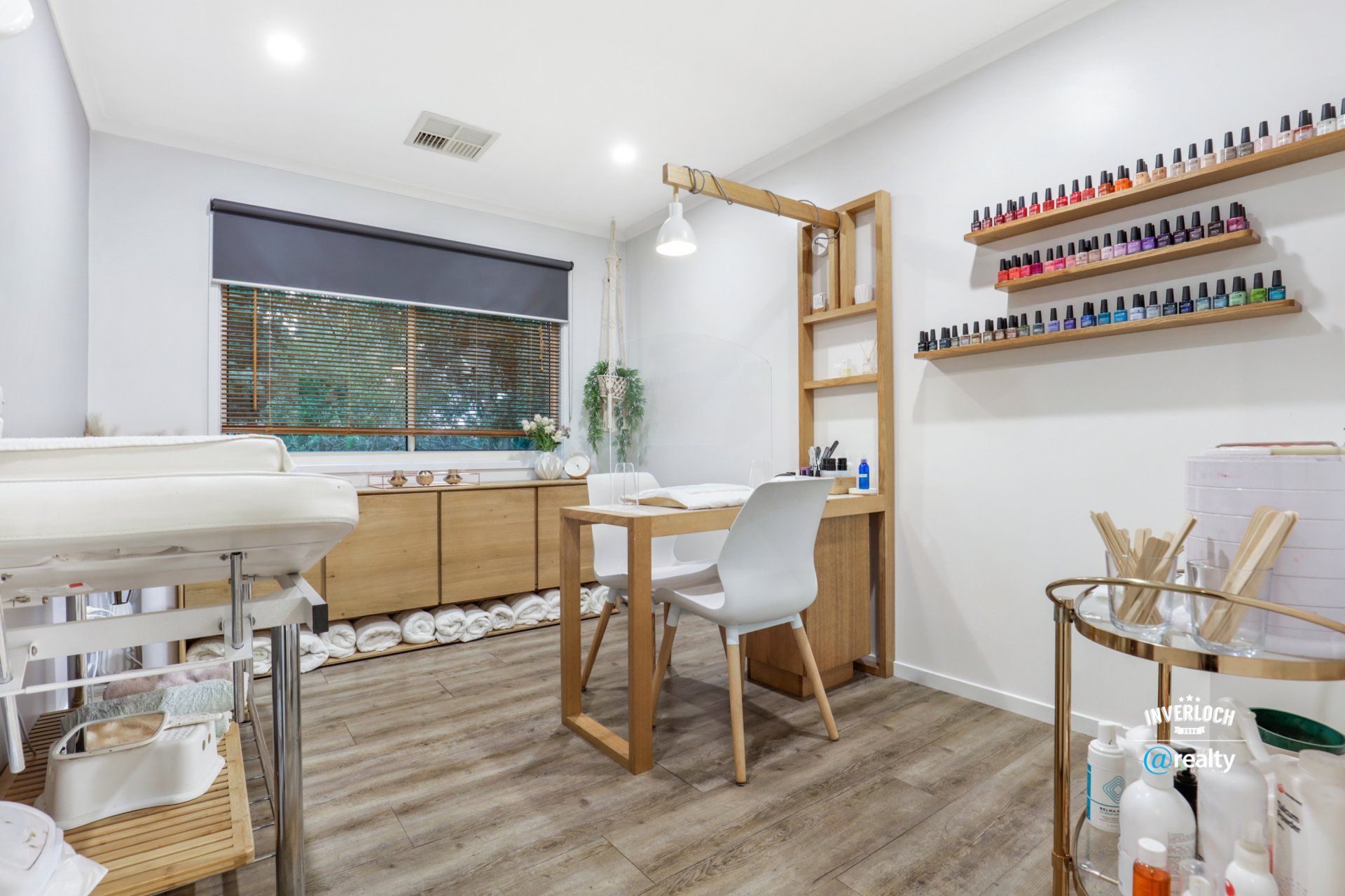 A room with a desk , chair , sink and shelves filled with nail polish.