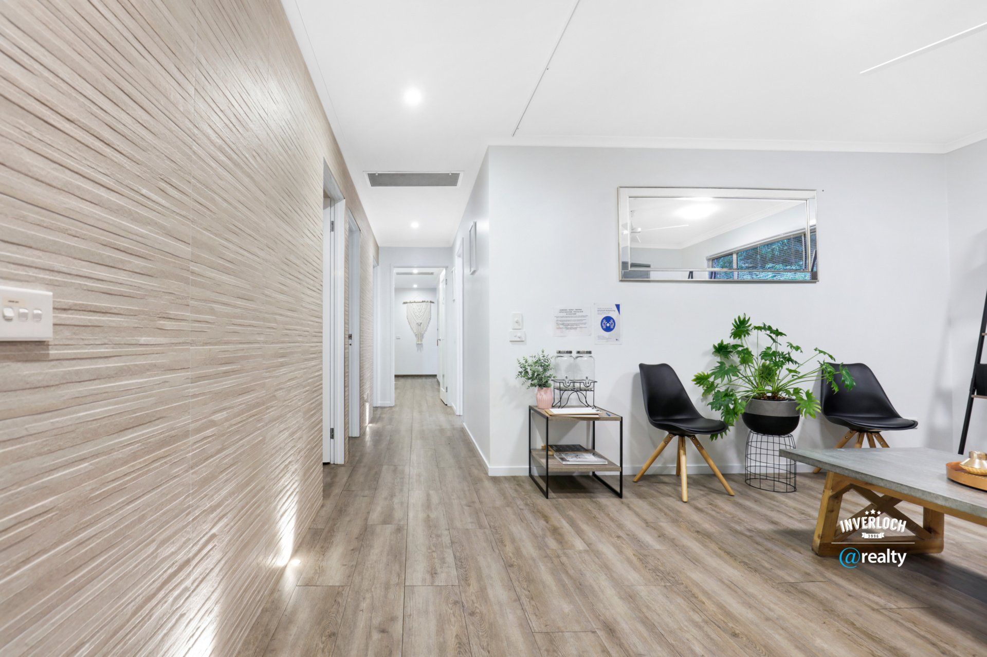 A waiting room with wooden floors , chairs , a table and a mirror.